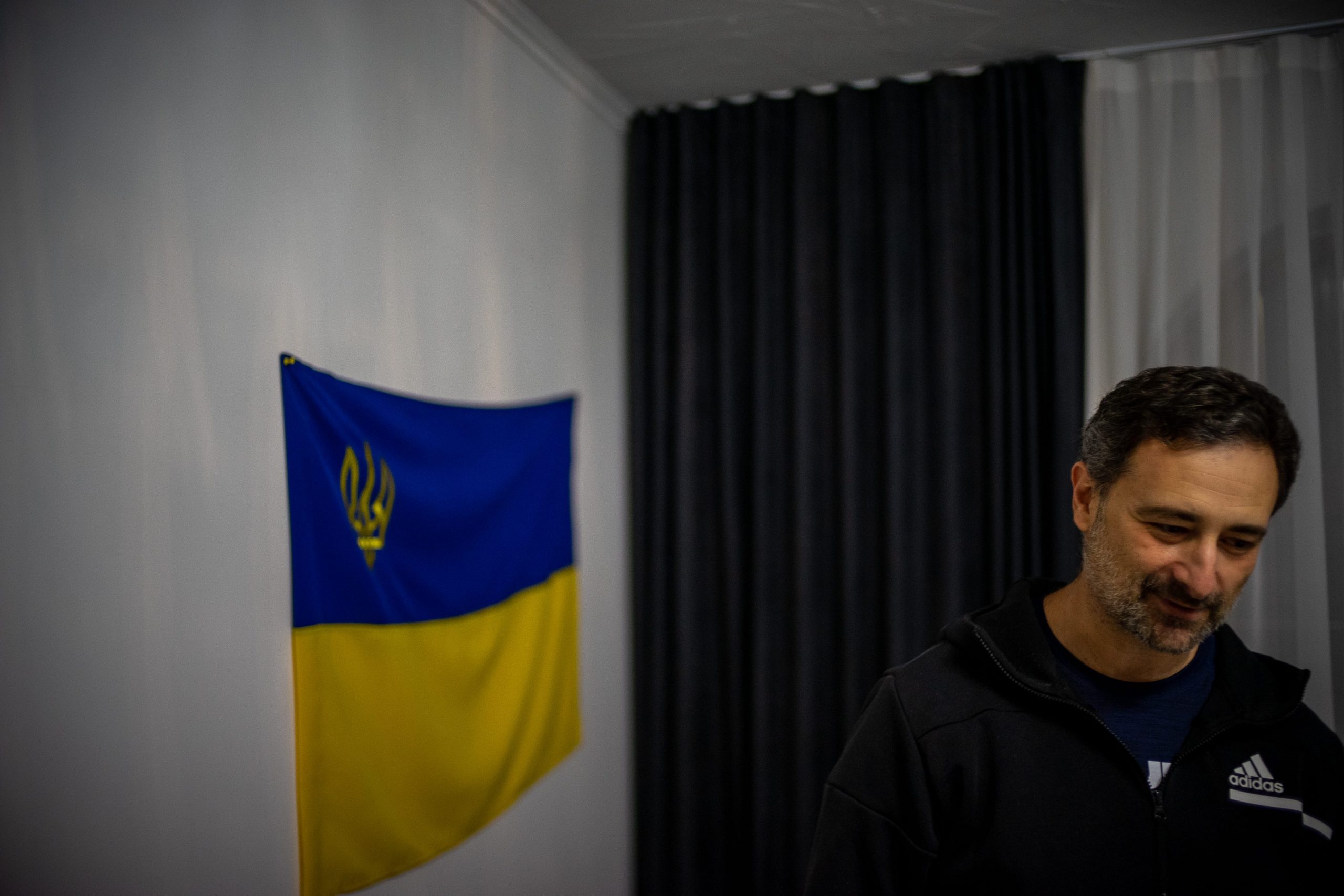 Man stands in a white room next to Ukraine flag.