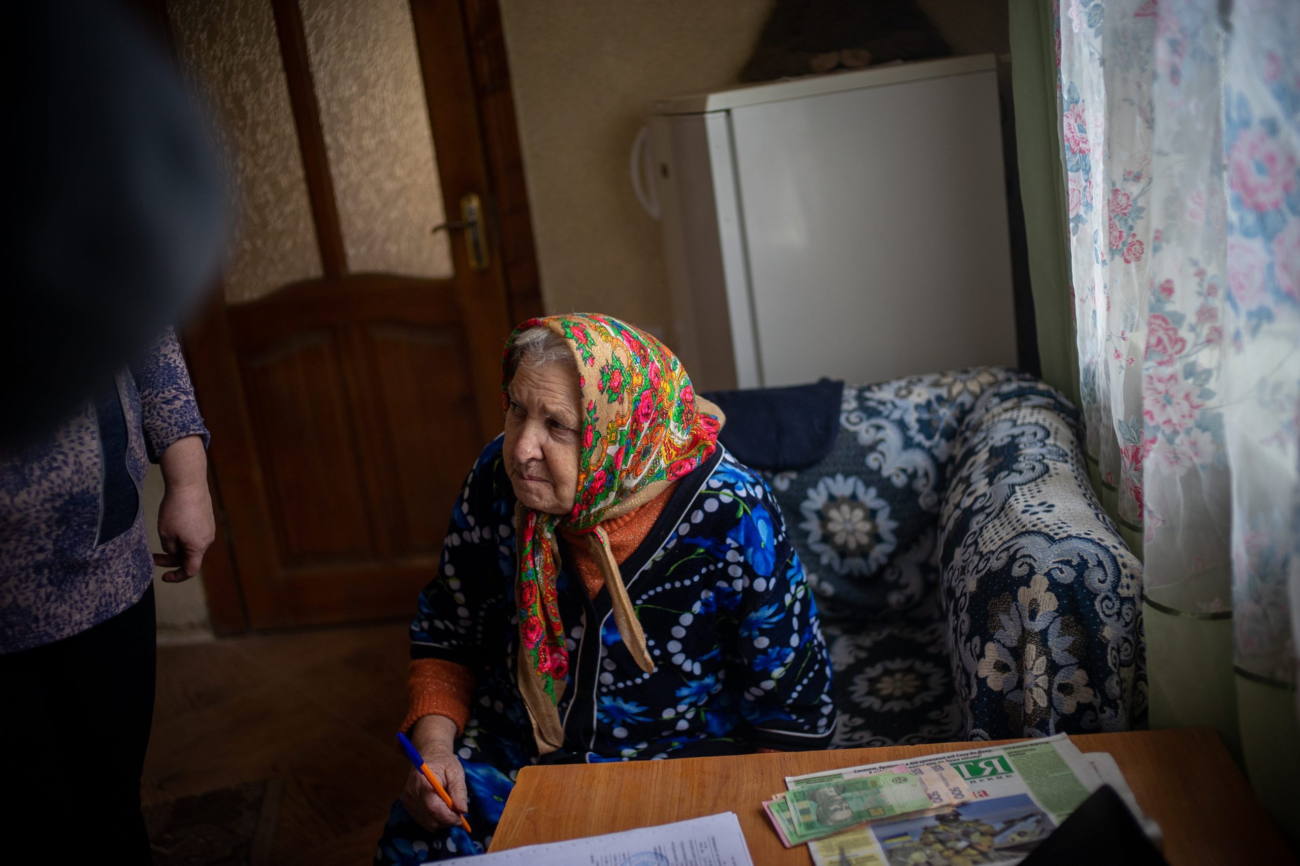 Elder woman sits in a chair in the kitchen.