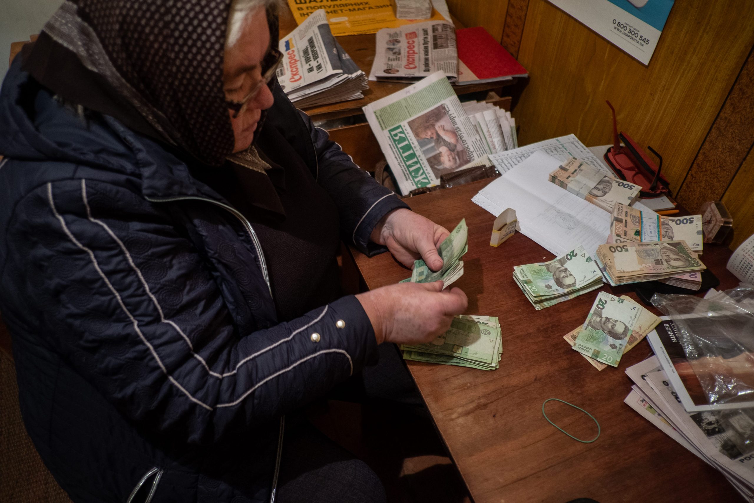 Stacks of money sit on a wooden table as a woman counts it.