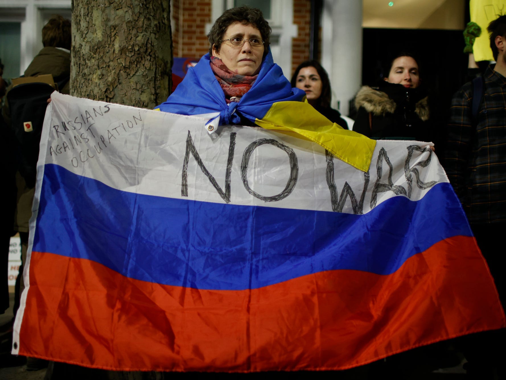 A woman holds a Russian flag with the message 'Russians Against Occupation — No War' as pro-Ukraine activists protest outside the Consular Section of the Russian Embassy in London, Saturday, Feb. 26, 2022.