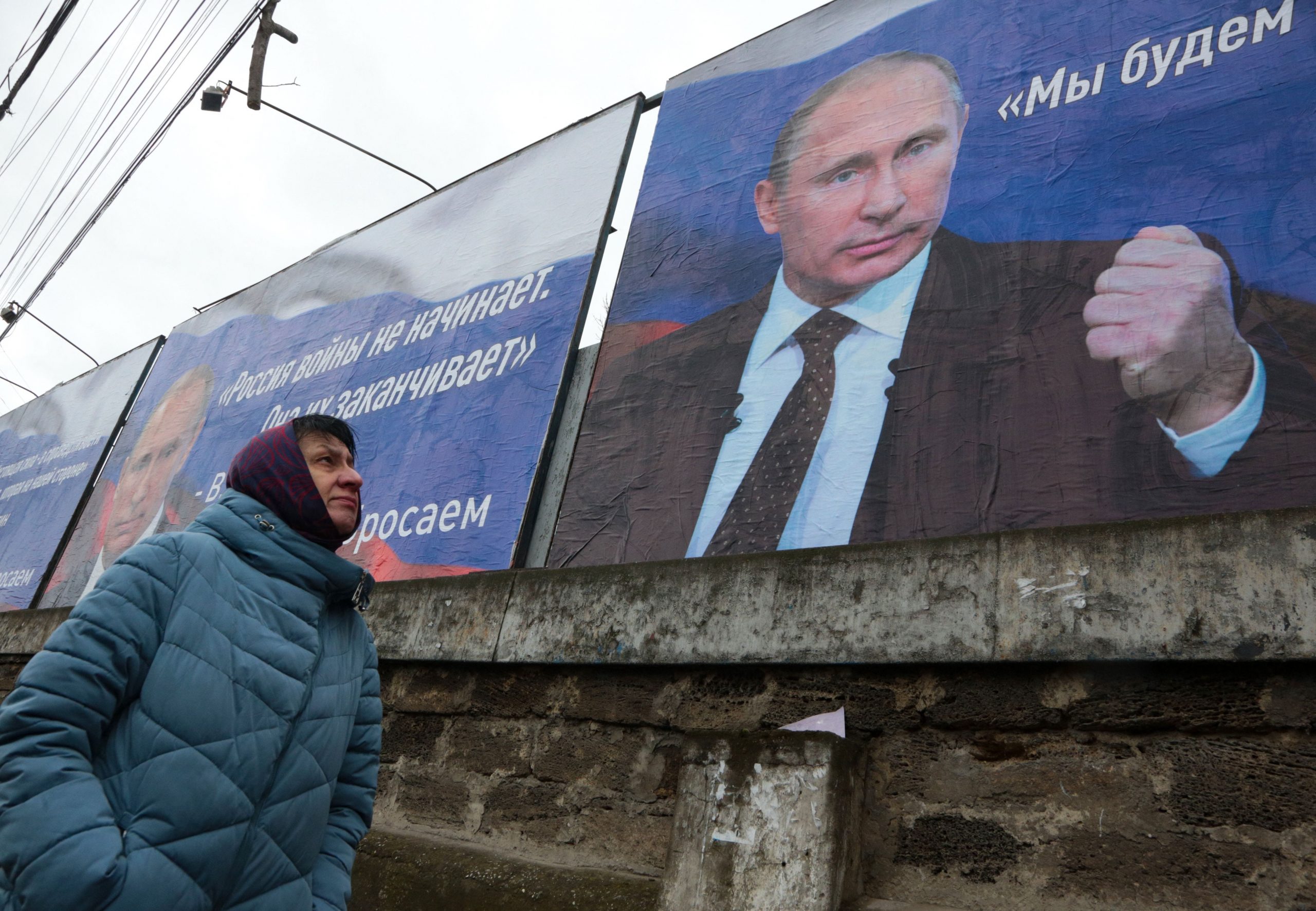 A woman walks past huge placards bearing images of Russian President Vladimir Putin and reading "Russia does not start wars, it ends them," in annexed Crimea