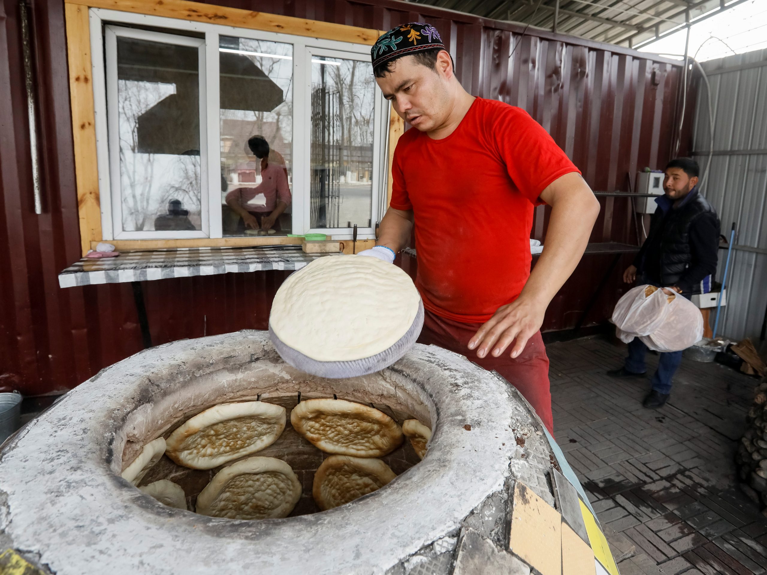Een arbeider stopt een brood in een tandyr kleioven in een bakkerij in het dorp Guldala, buiten Almaty, Kazachstan.