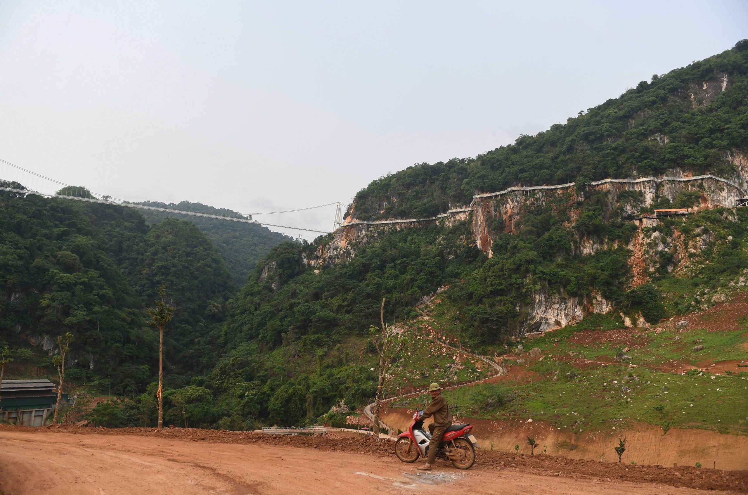 A man rides his motorbike under the Bach Long glass bridge in Moc Chau district in Vietnam&#39;s Son La province on April 29, 2022