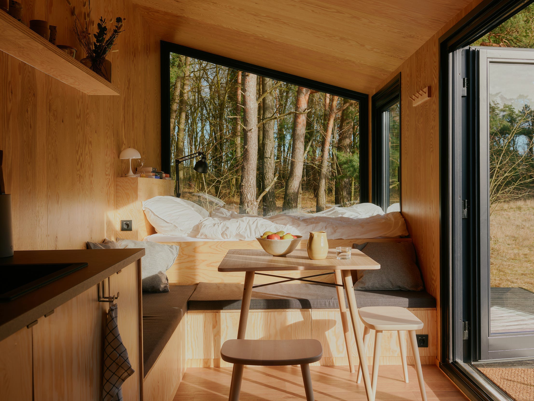 Een bed, keuken, tafel met stoelen en ramen met zicht op de natuur.