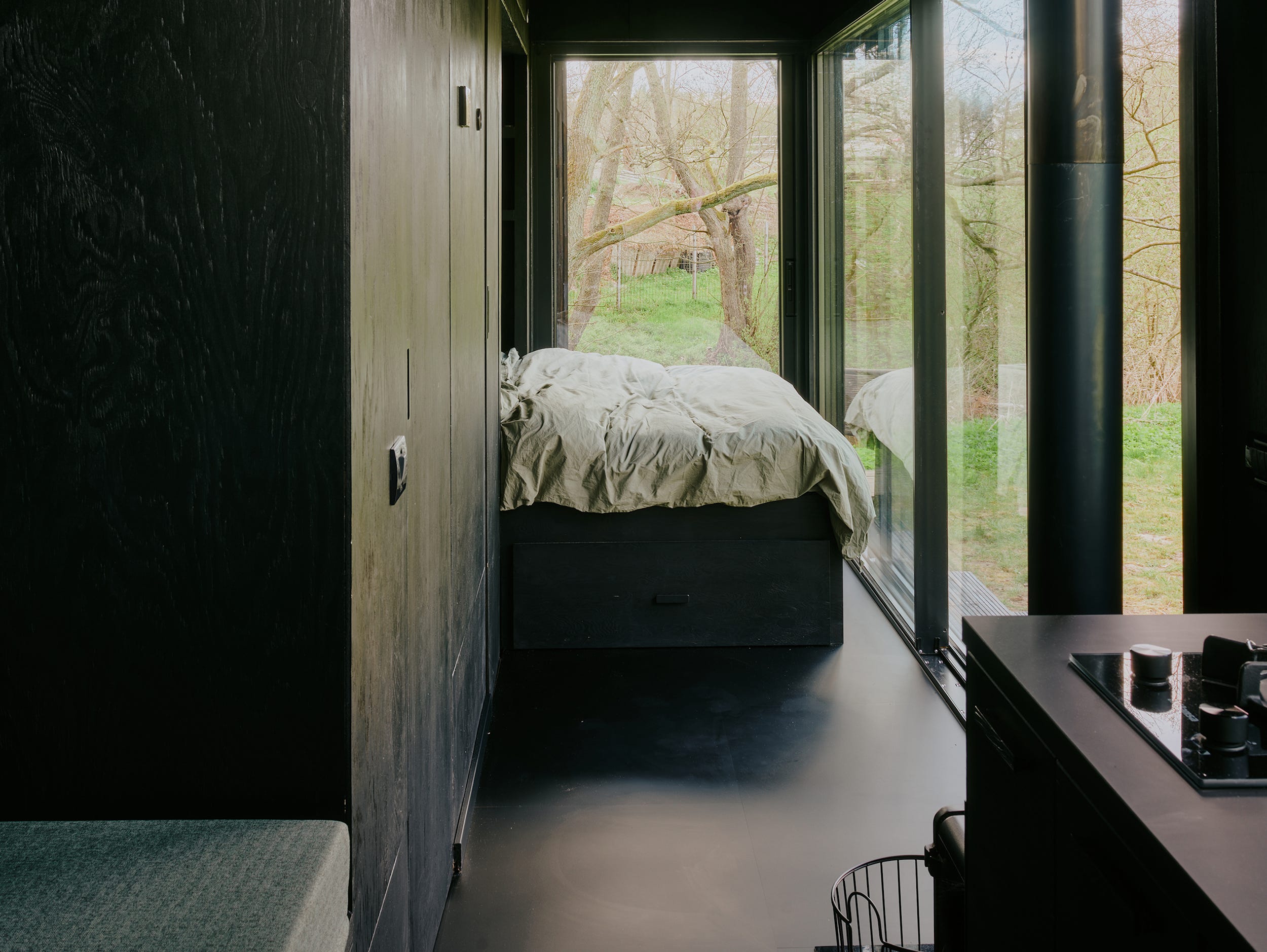 Een bed, keuken, dagbed en ramen met uitzicht op de natuur.