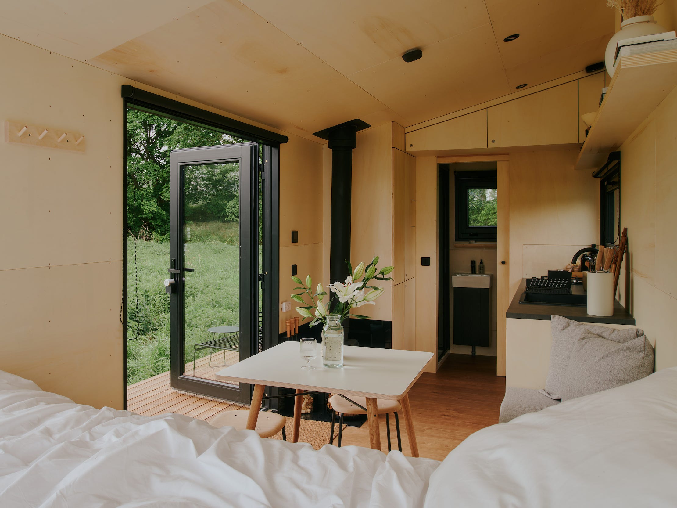 Een kijkje in een Raus-huisje met een bed, eettafel, keuken en ramen met uitzicht op de natuur.