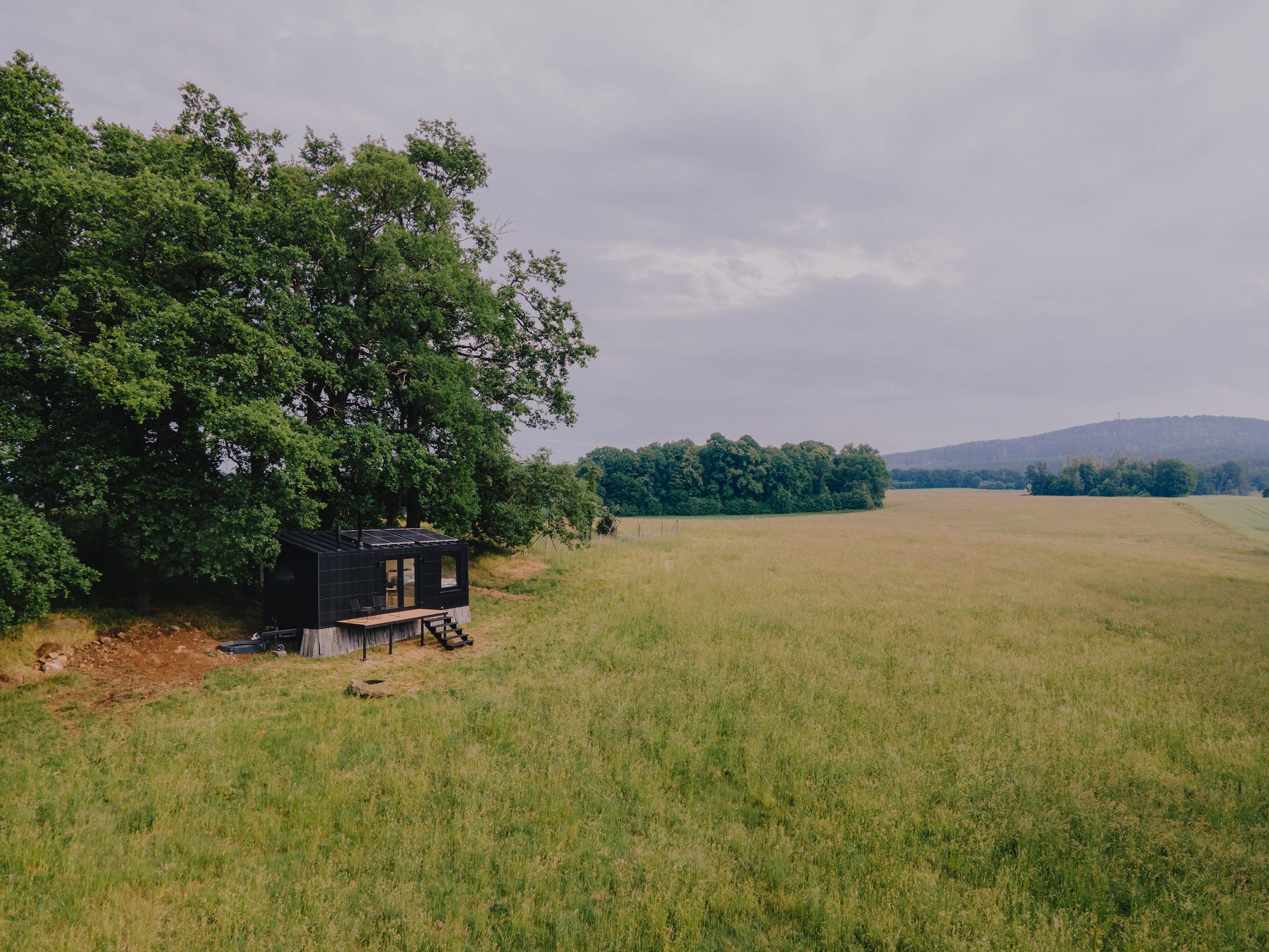 Een Raus-hut buiten in de natuur, omringd door bomen en een open veld