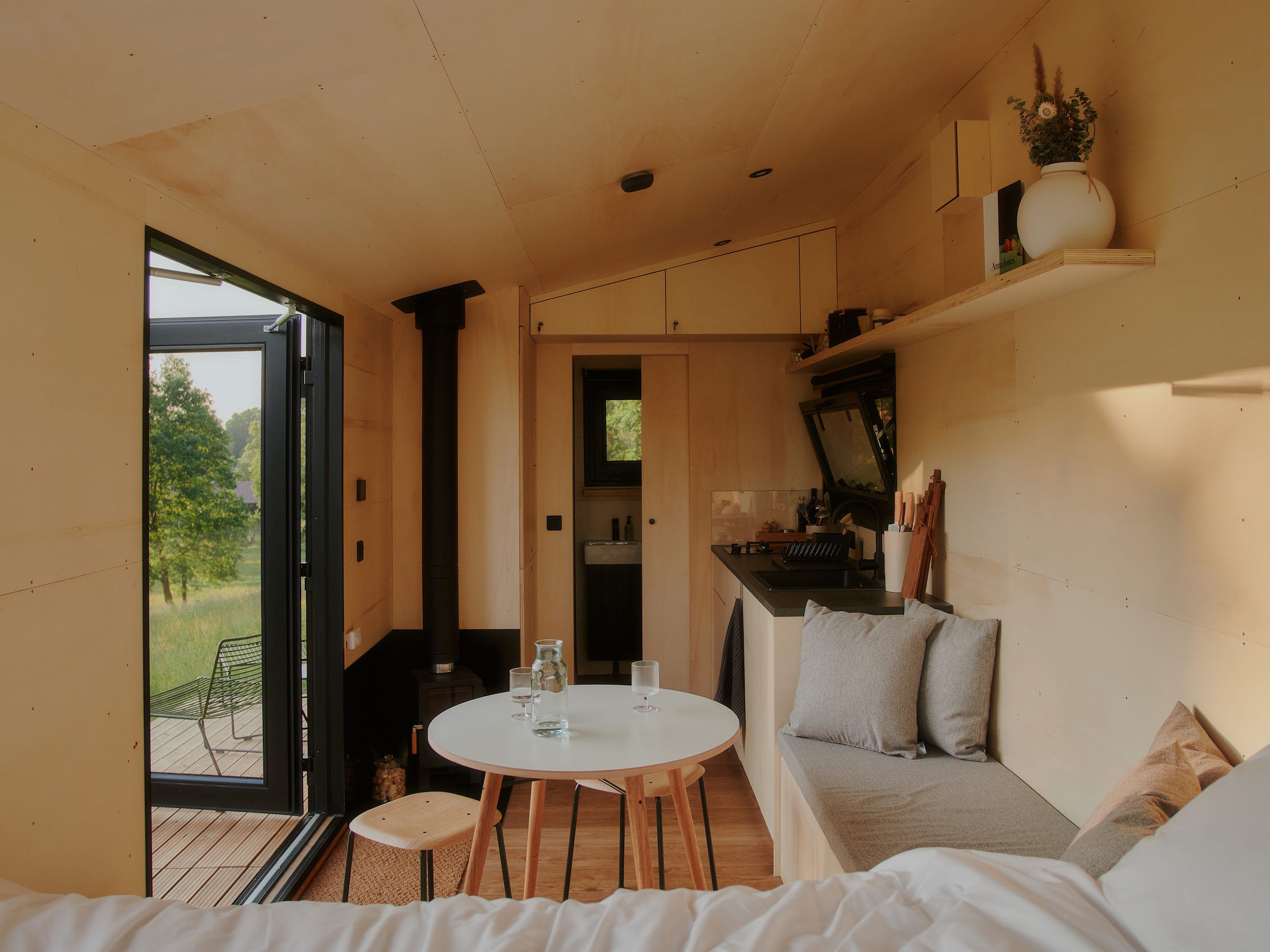 Een kijkje in een Raus-hut met een bed, eettafel, keuken en ramen met uitzicht op de natuur.
