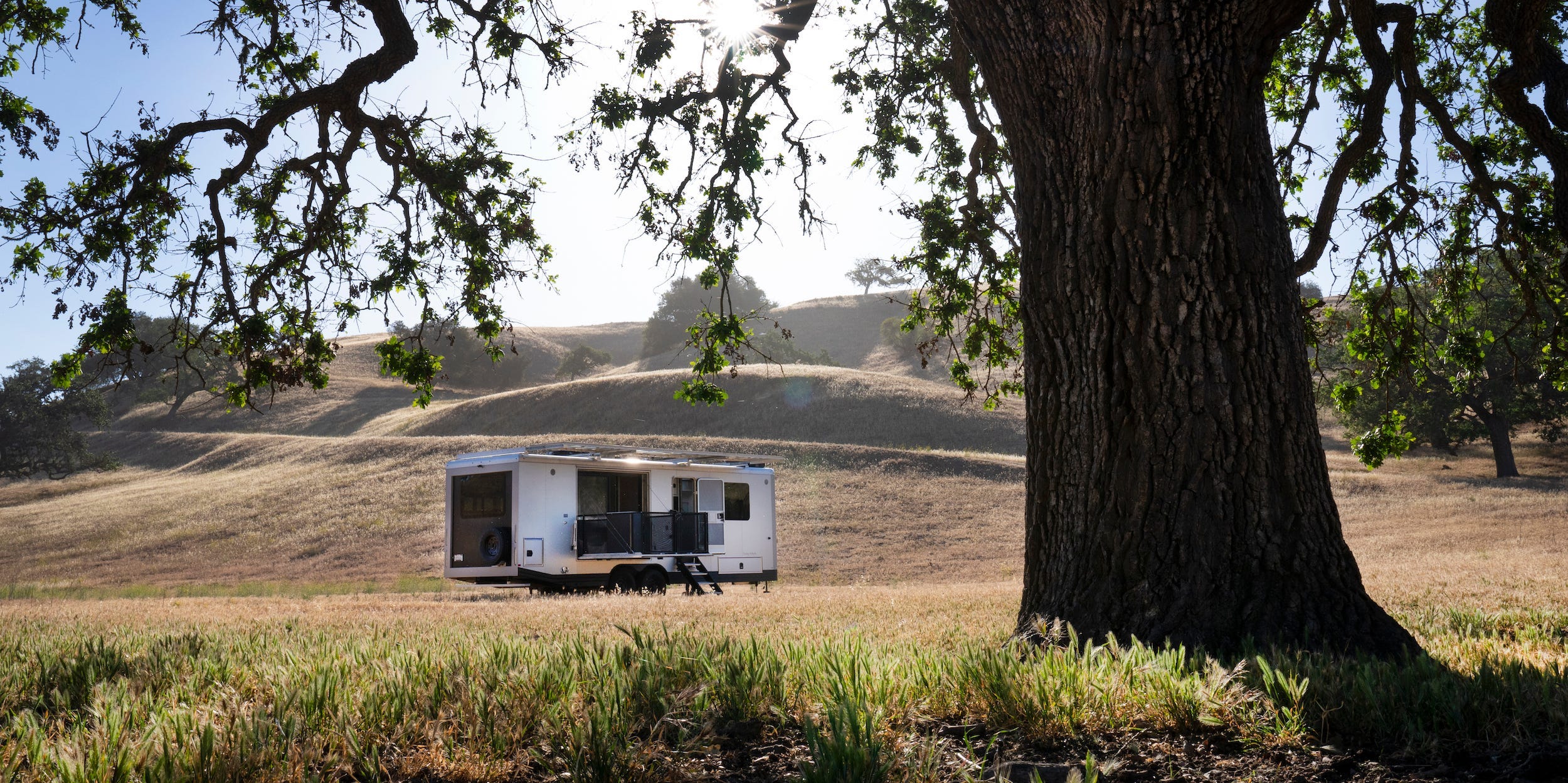 De buitenkant van de reiswagen zoals die op een bruin veld bij een boom staat.