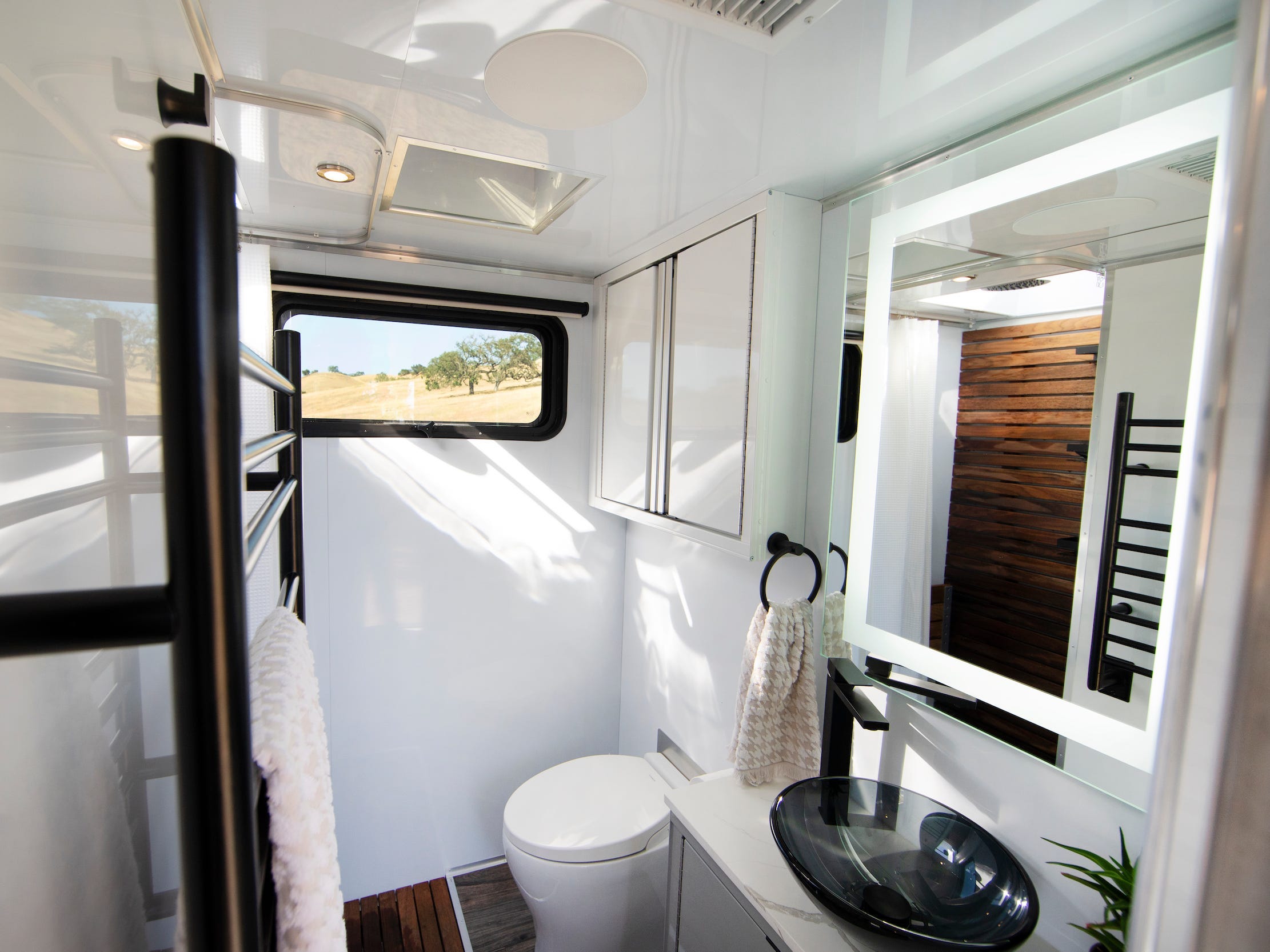 Een badkamer met een raam, handdoekenrek, spiegel, wastafel, toilet.