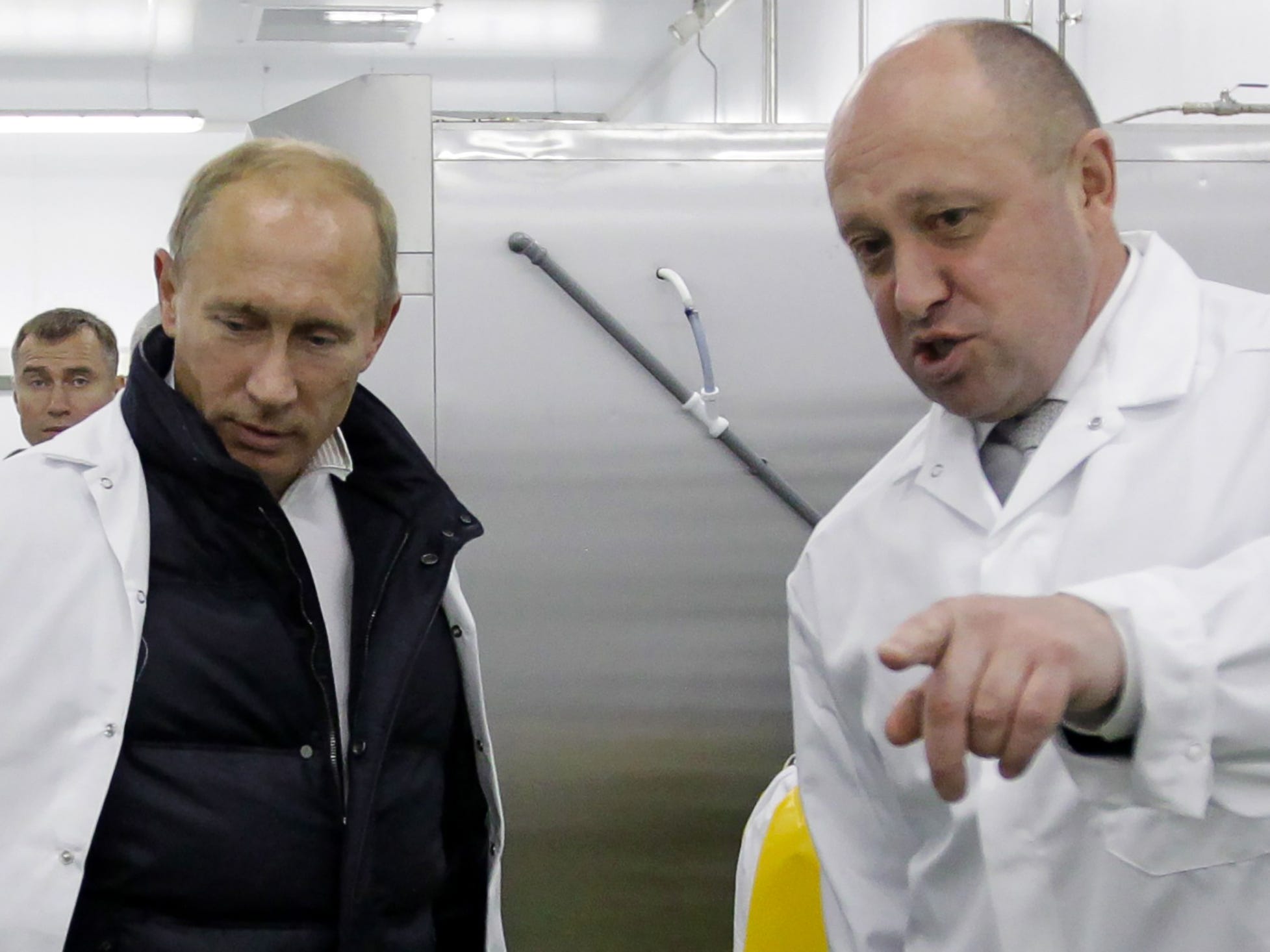 Putin and Prigozhin in white coats, with the latter pointing at something off-camera