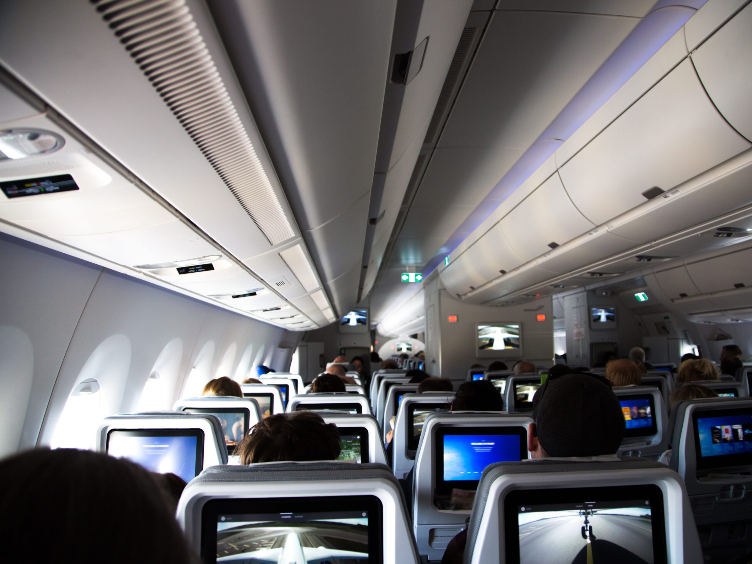 Inside of a long distance new airplane with passengers sitting and resting during a long flight with picture taken from the back of the airplane