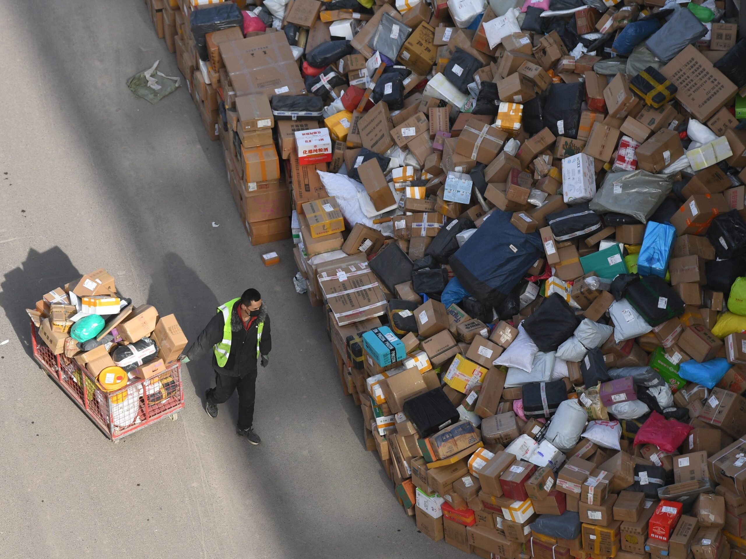 Multicolored packages are piled up in a massive mound while a delivery work moves one load away from the pile at a sortation center in China.