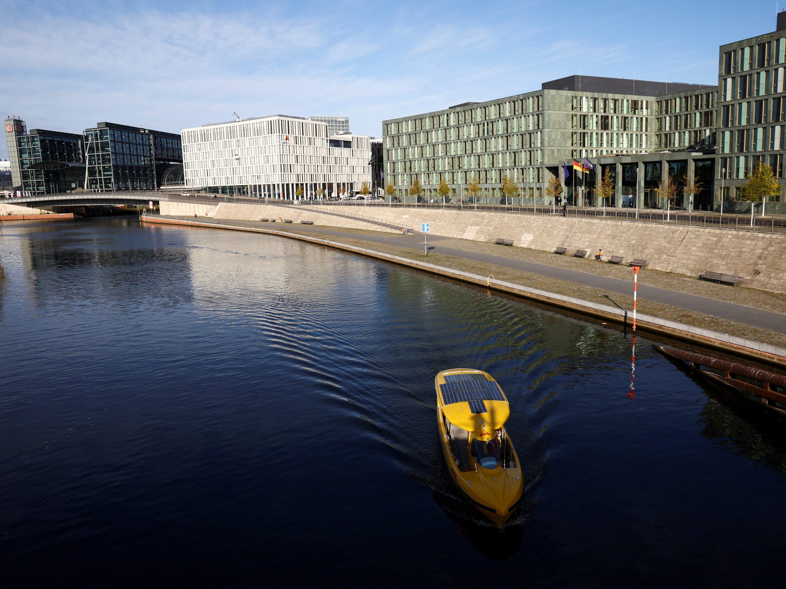 A bright yellow boat goes down a very still river in front of office buildings in Berlin, Germany.