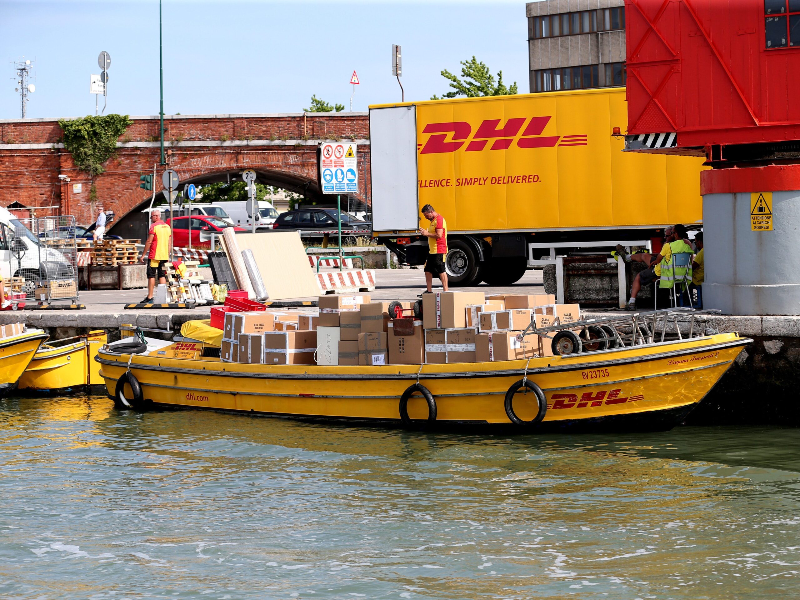 A yellow DHL boat full of packages is parked dockside in Venice, Italy.