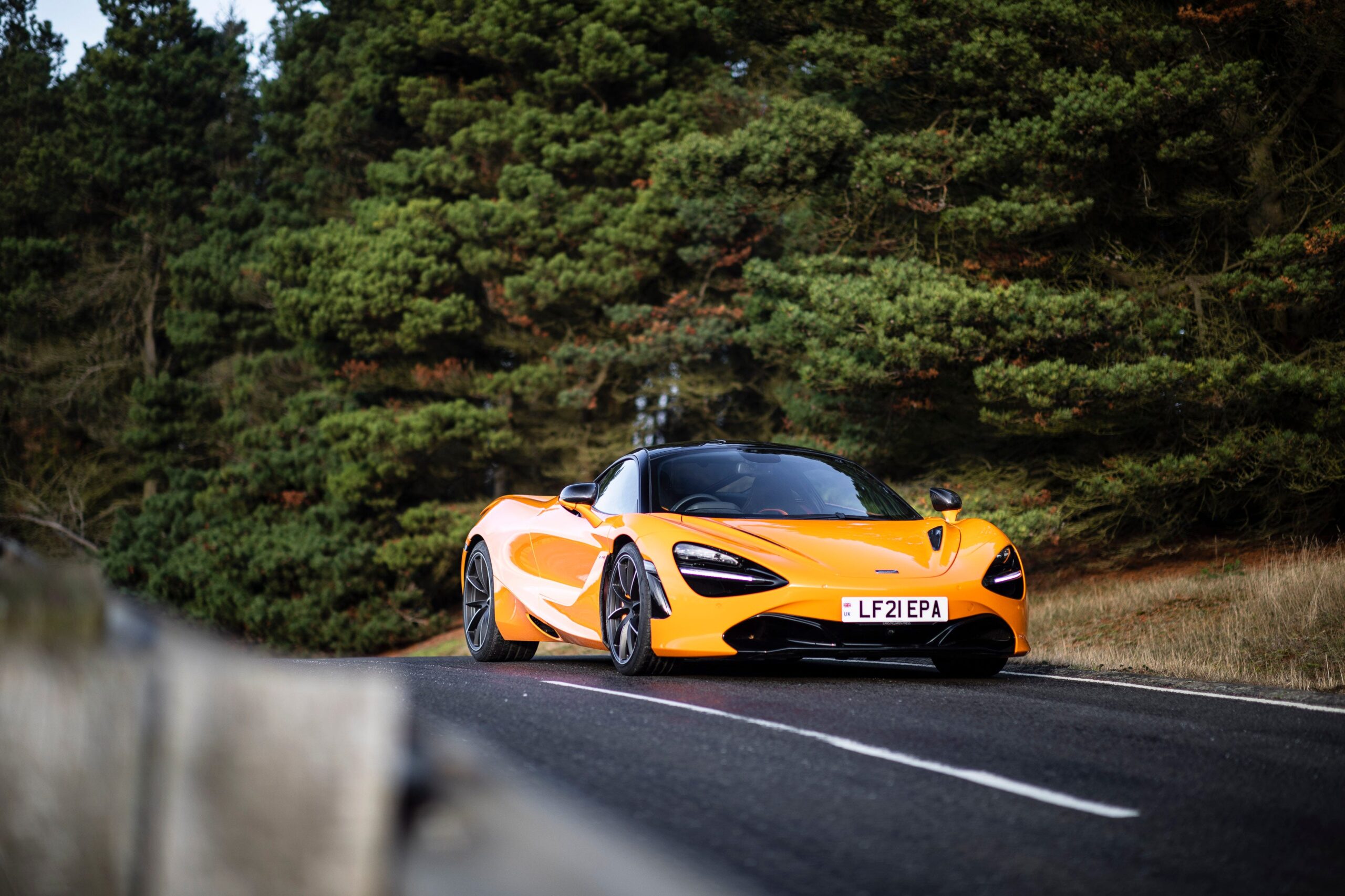An orange McLaren 720S on a wooded road.