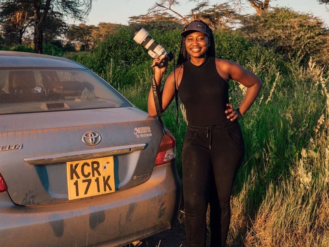 A woman standing with a camera next to a car.