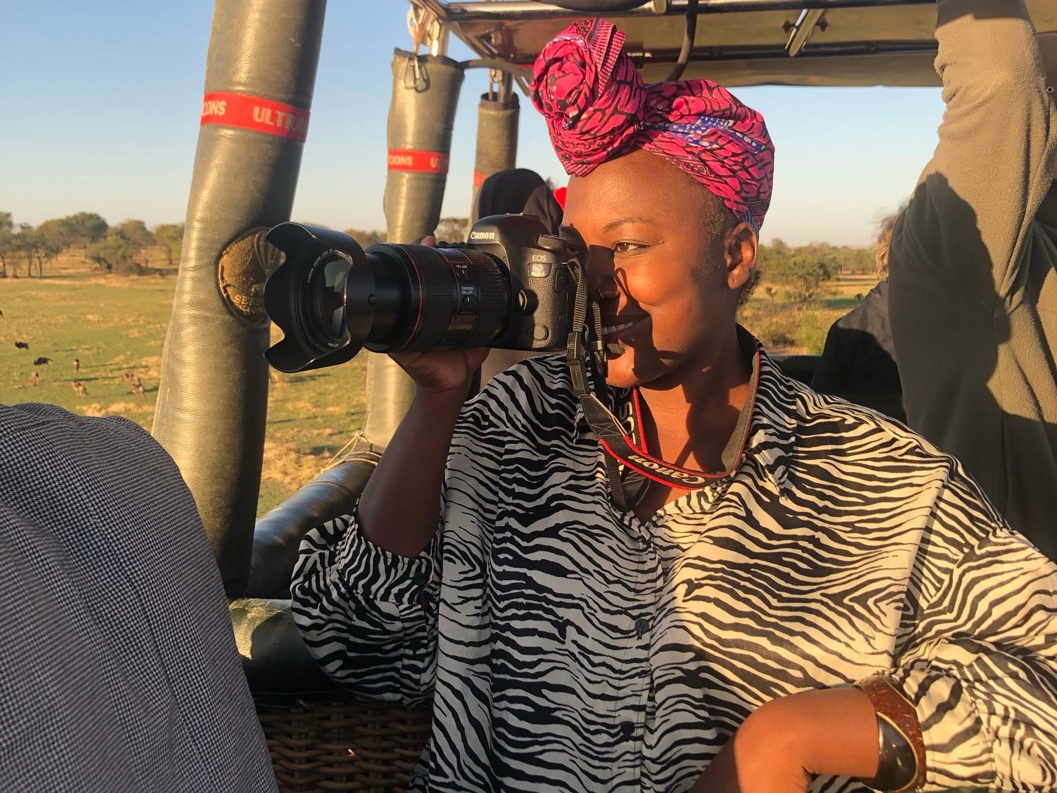 A woman wearing a zebra print shirt on an open jeep looking into a camera.