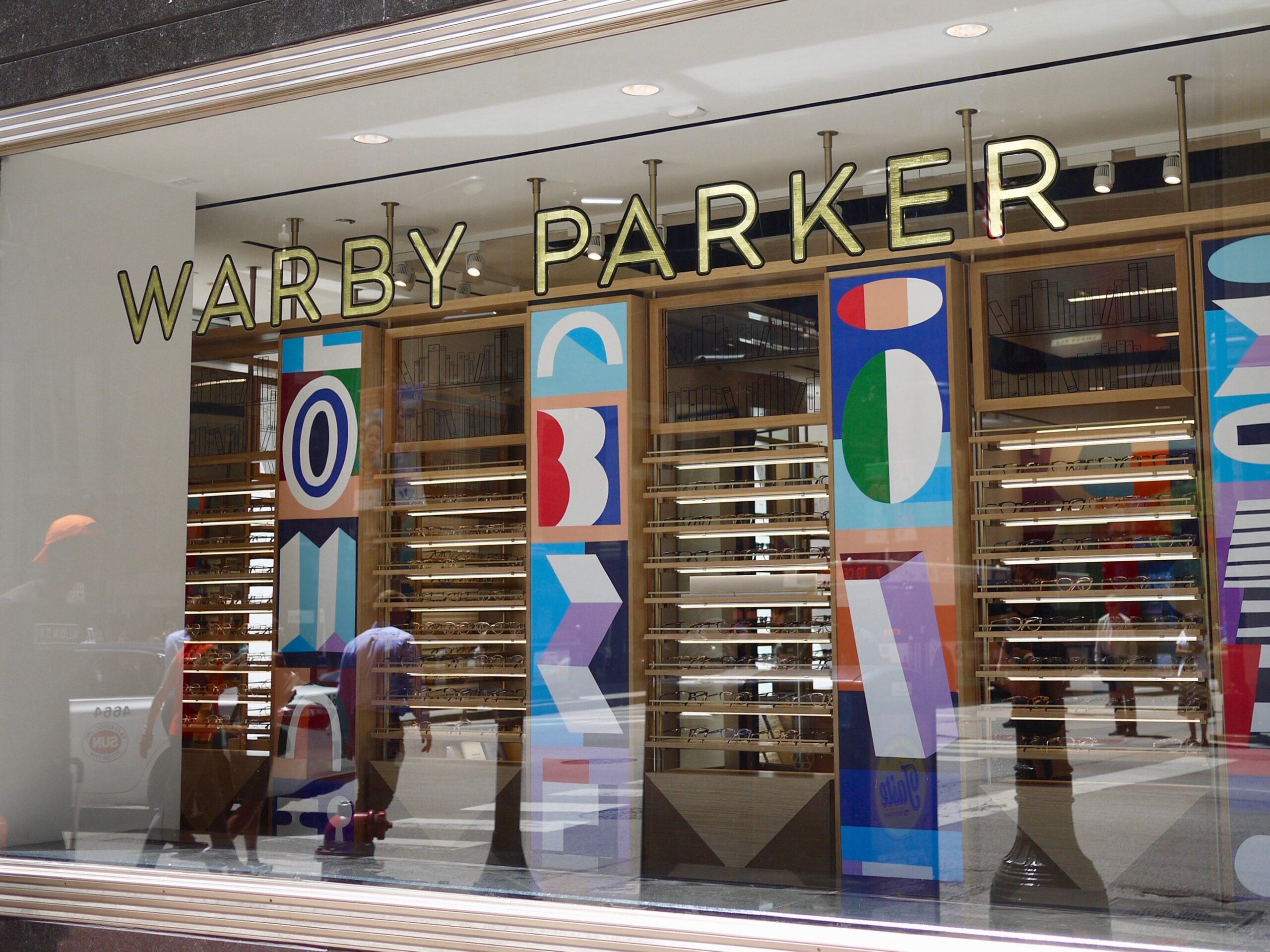 A street window looking into a Warby Parker store with artistic patterns on the walls.