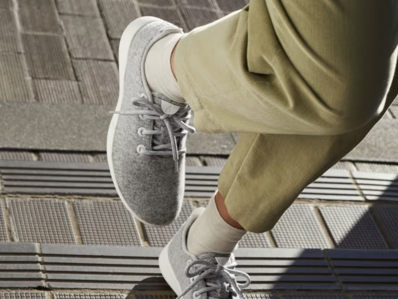 A model&#39;s legs from the thigh down. They are wearing green trousers and AllBirds Wool Runners.