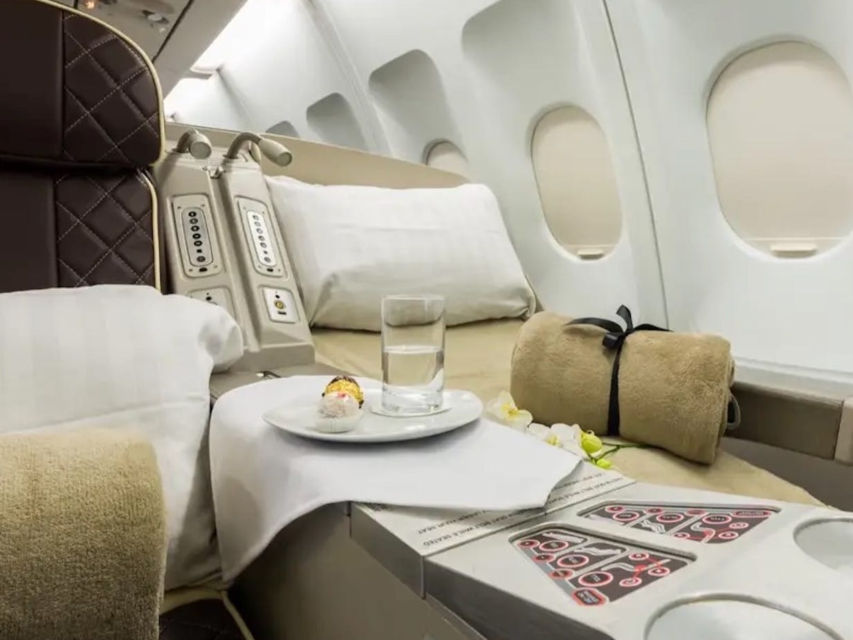 AirX Charters' A340 business class seat in lie-flat mode with a pillow and yellow blanket.