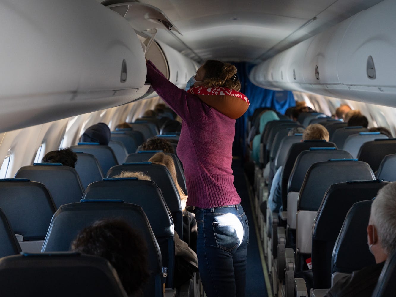 A traveler wearing a neck pillow access a plane's overhead bins.