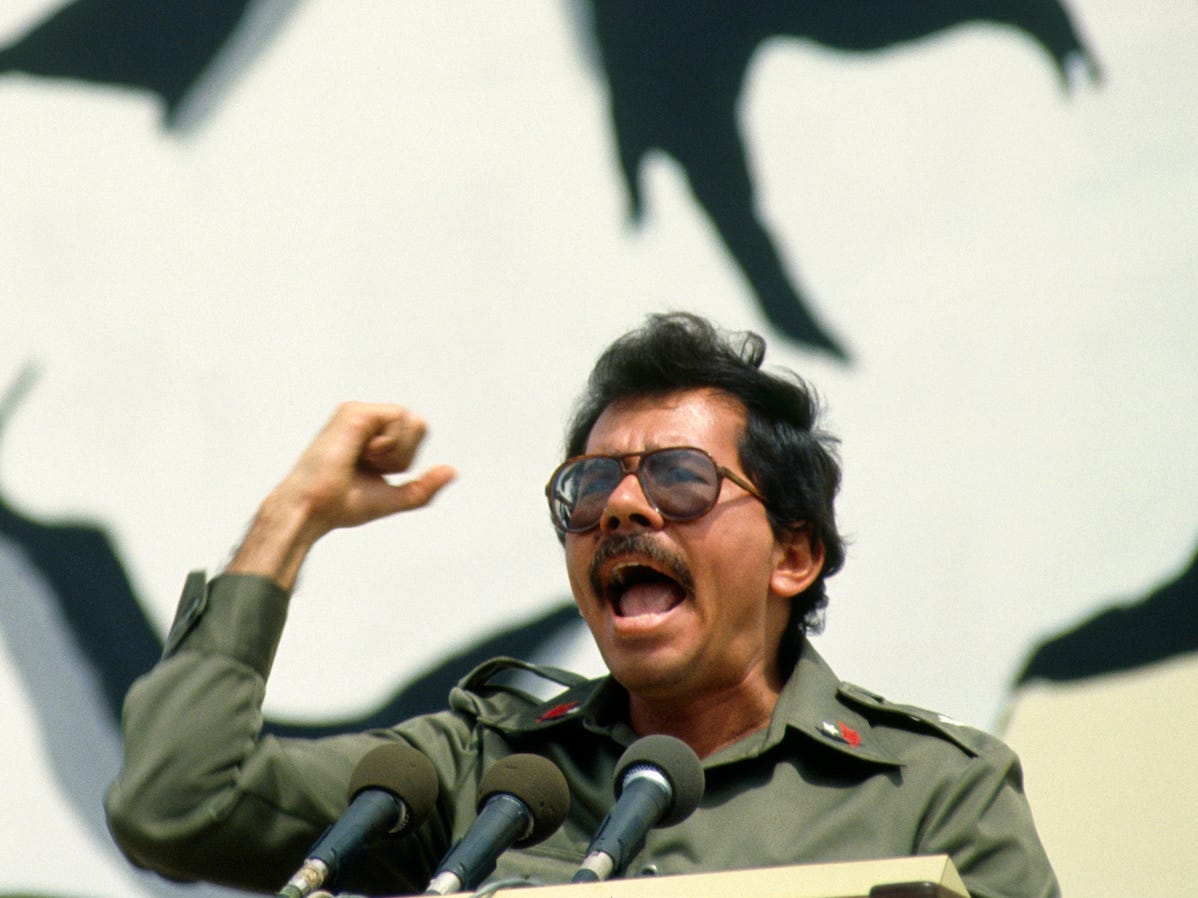 Daniel Ortega in 1984 schreeuwend in een microfoon voor een enorme muurschildering.