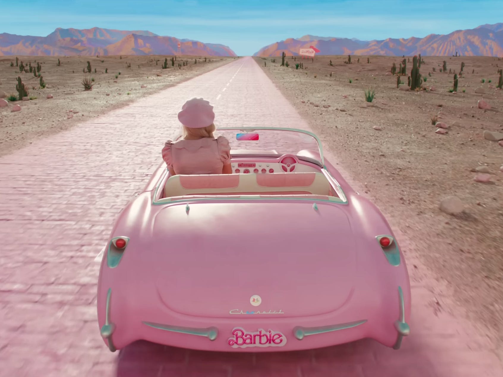 Margot Robbie as Barbie, driving along a pink brick road, in &#34;Barbie.&#34;