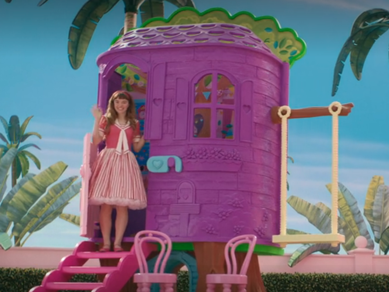 skipper in barbie, a teenage girl standing on the front steps of a purple plastic treehouse