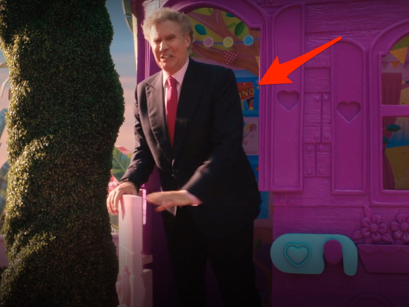 will ferrel walks out of a purple treehouse in barbie. theres a red arrow pointing to an uno deck on the wall behind him