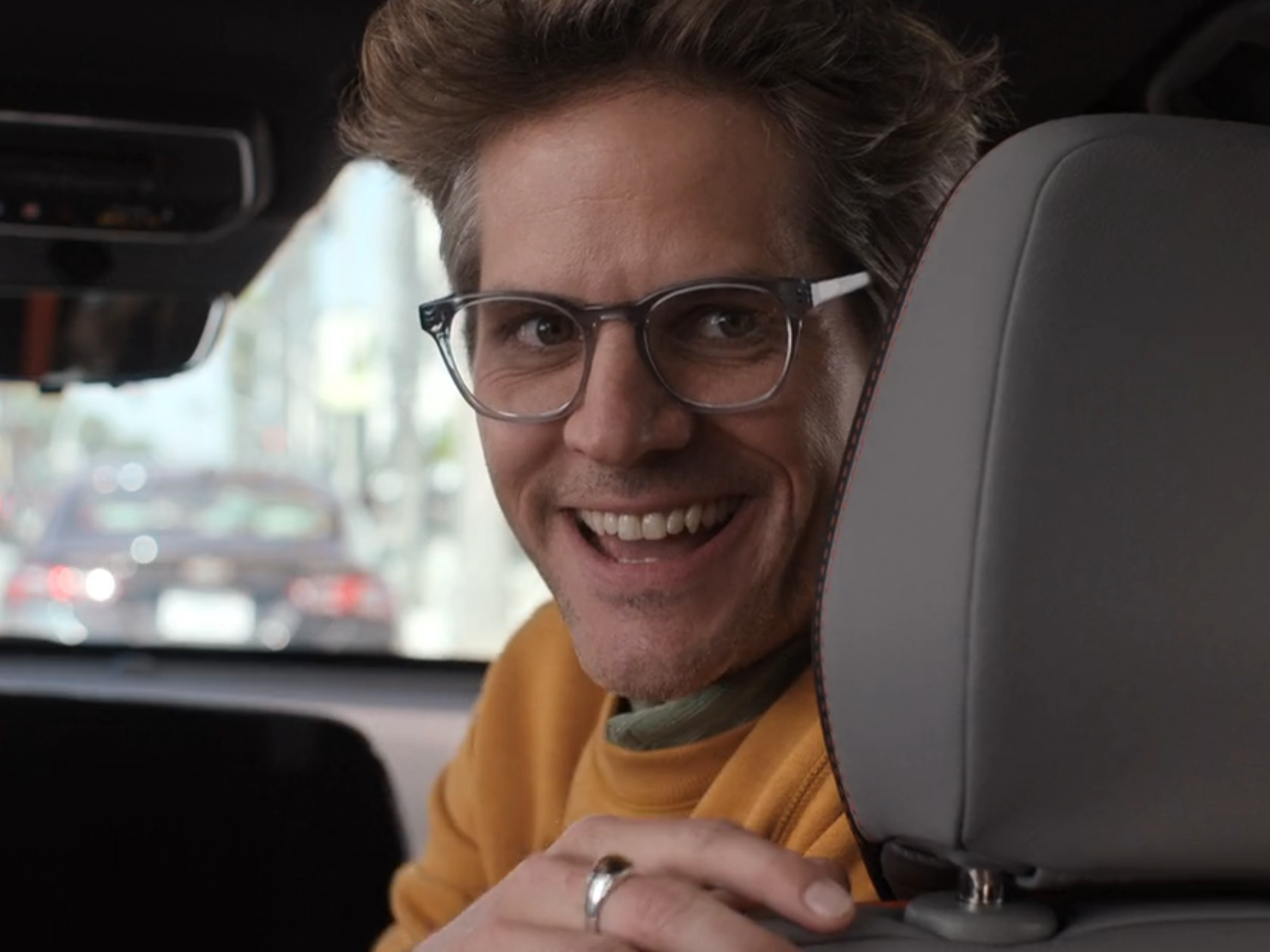 Ryan Piers Williams in barbie as gloria&#39;s husband, smiling from the front seat of a car