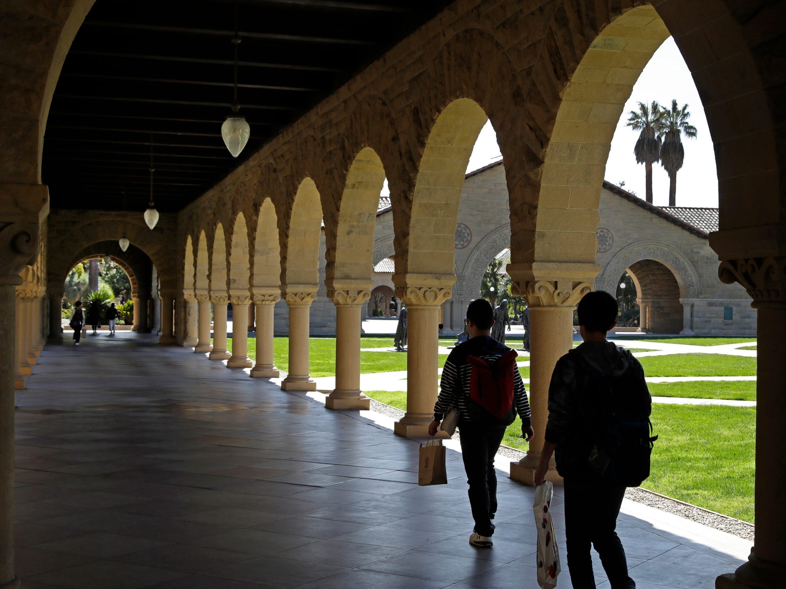 People walking next to columns and arches on the campus of Stanford University.