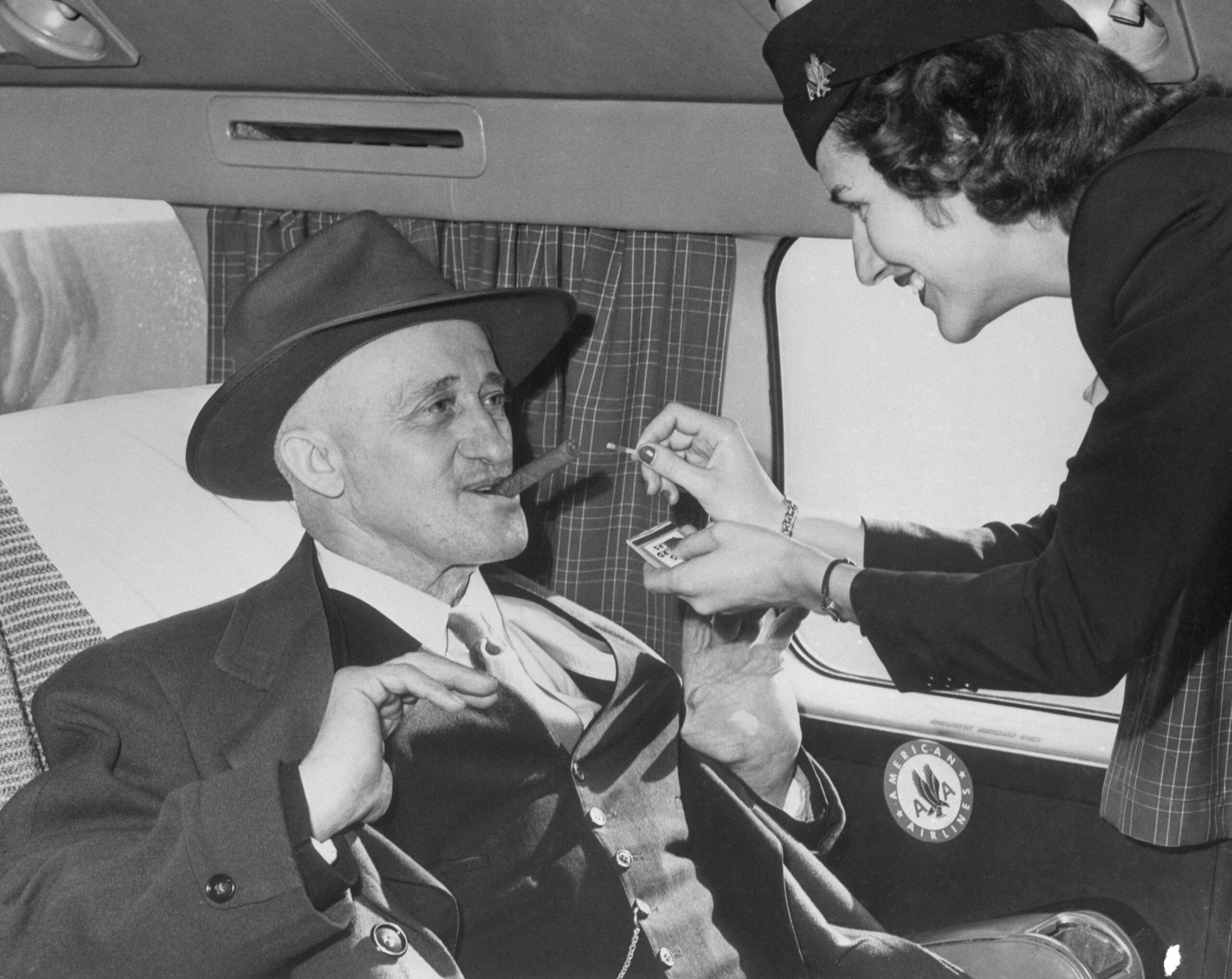 A flight attendant lights a man's cigar on a plane in 1949