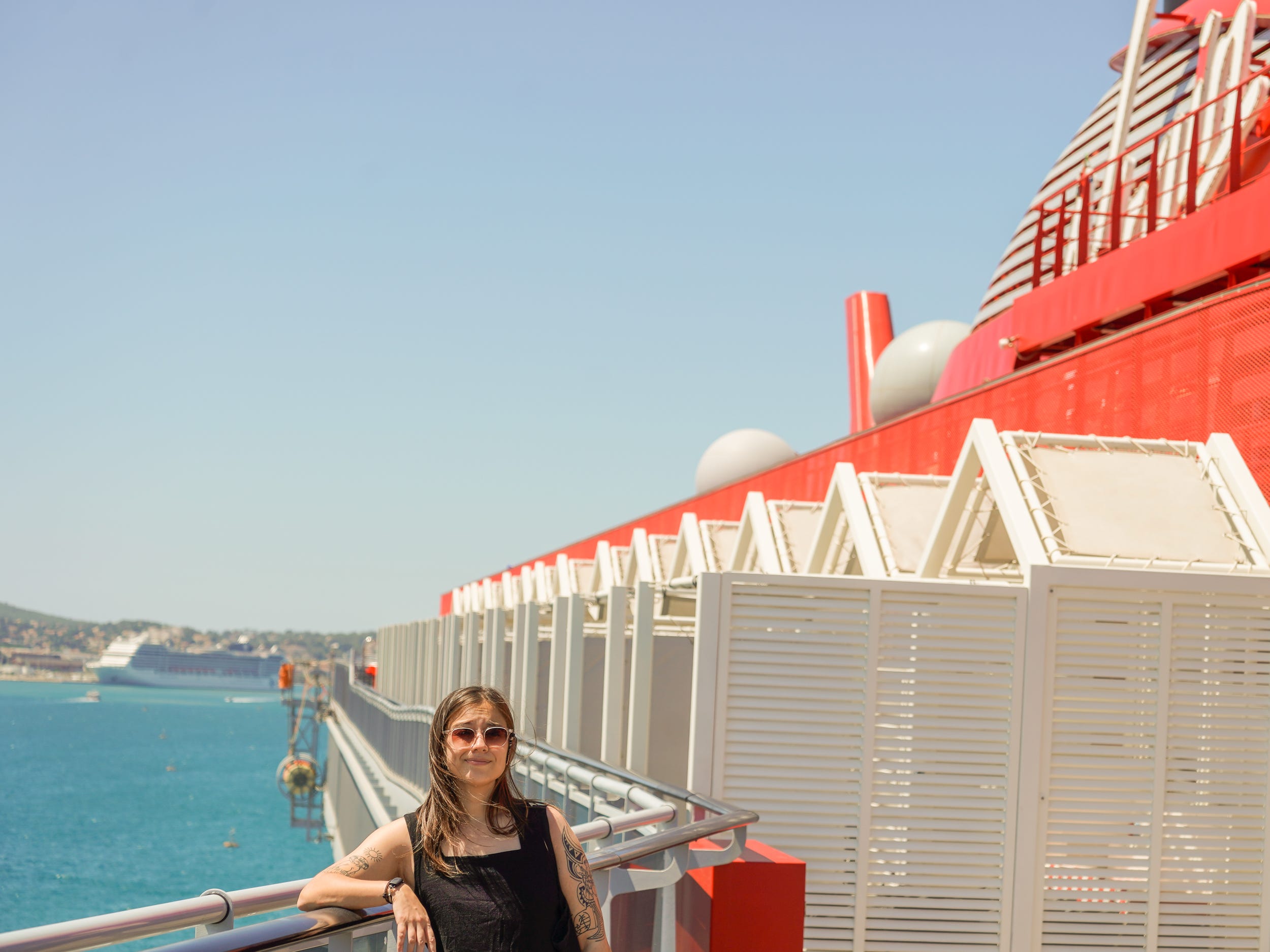 The author leans against a railing on a red cruise ship with water on the left on a clear day with blue skies.