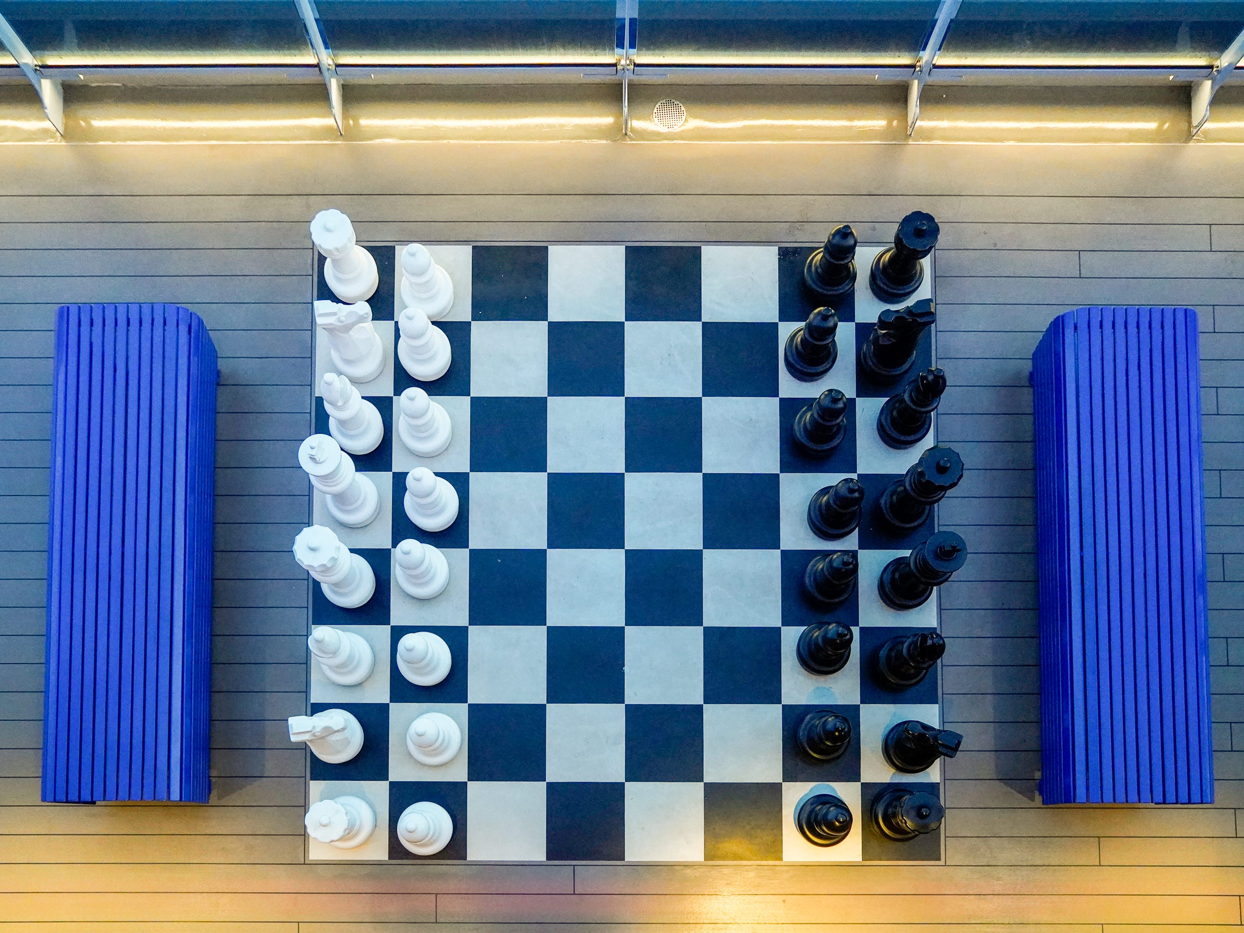 An aerial view of a large chess set between two blue benches on a cruise ship deck