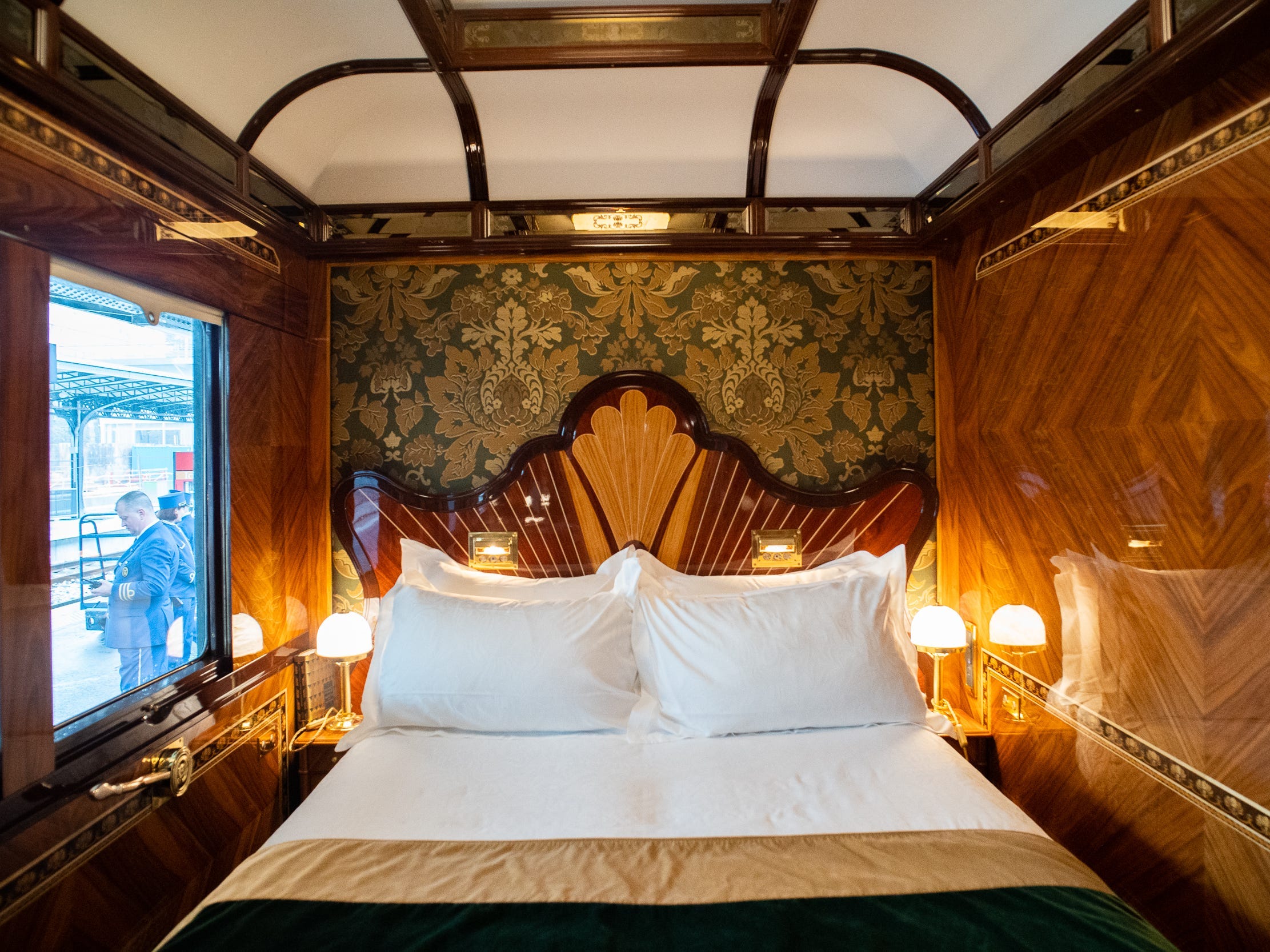A luxurious train cabin with wooden walls and a fancy double bed with a decorative headboard
