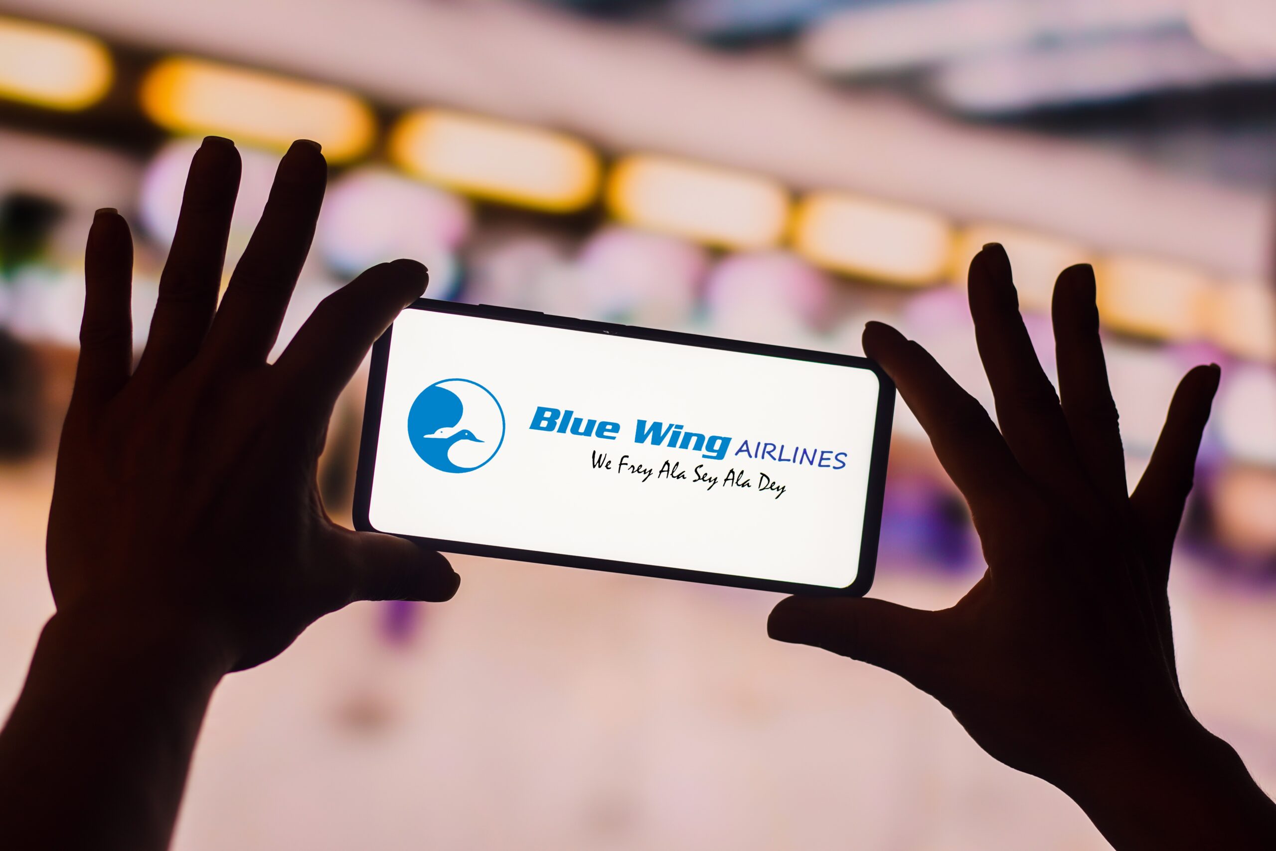 Logo van de Surinaamse luchtvaartmaatschappij Blue Wing Airlines op een mobiele telefoon. Foto: Rafael Henrique / SOPA Images / Sipa USA