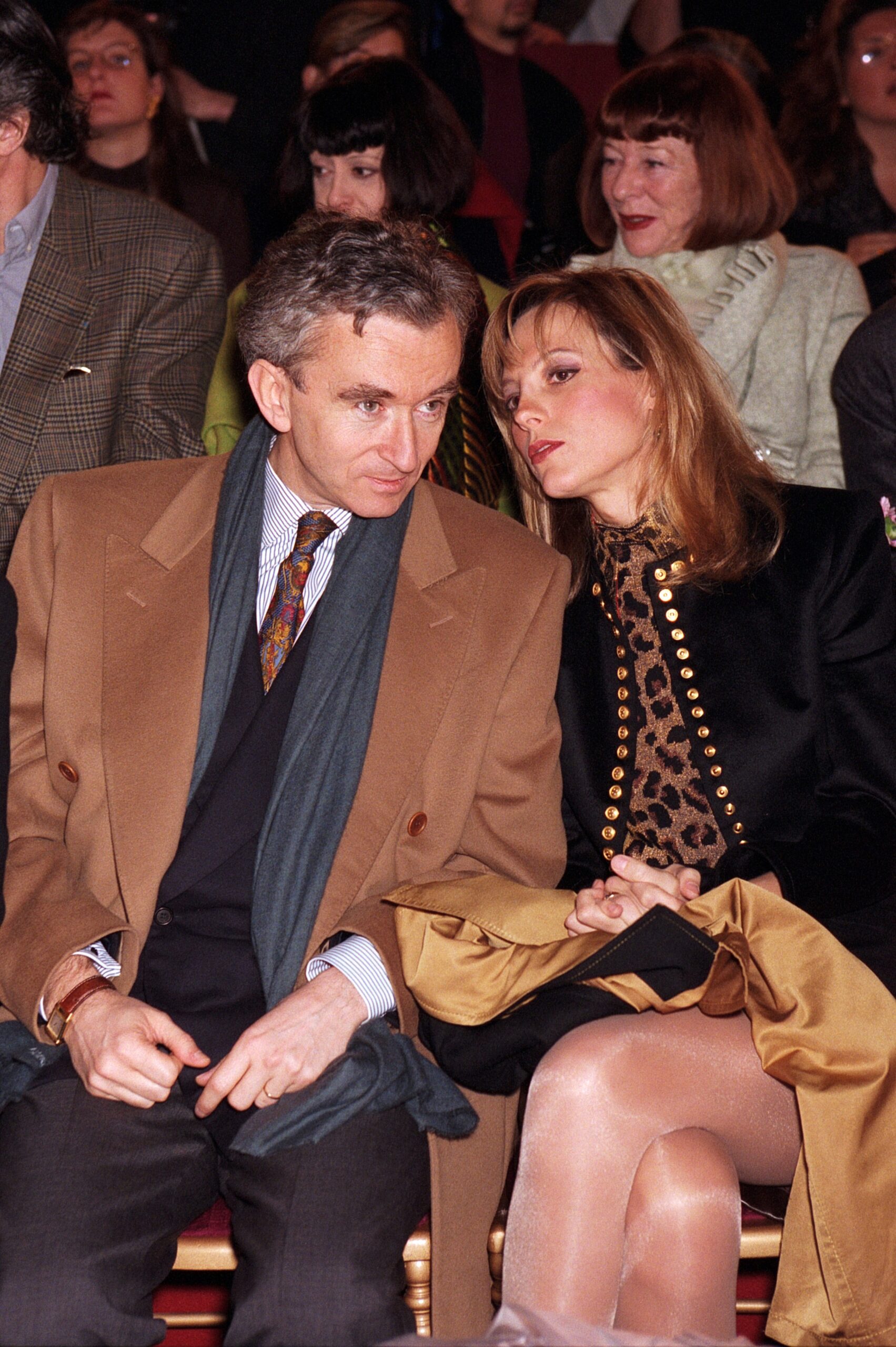 Bernard Arnault wearing a camel colored coat and gray suit  sat next to his wife