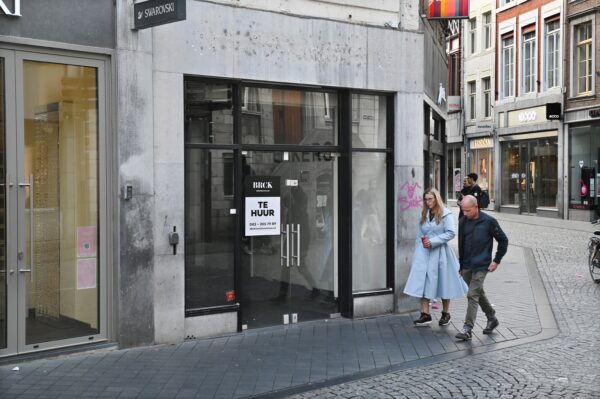 Winkelend publiek loopt langs een leegstaand winkelpand in Maastricht.