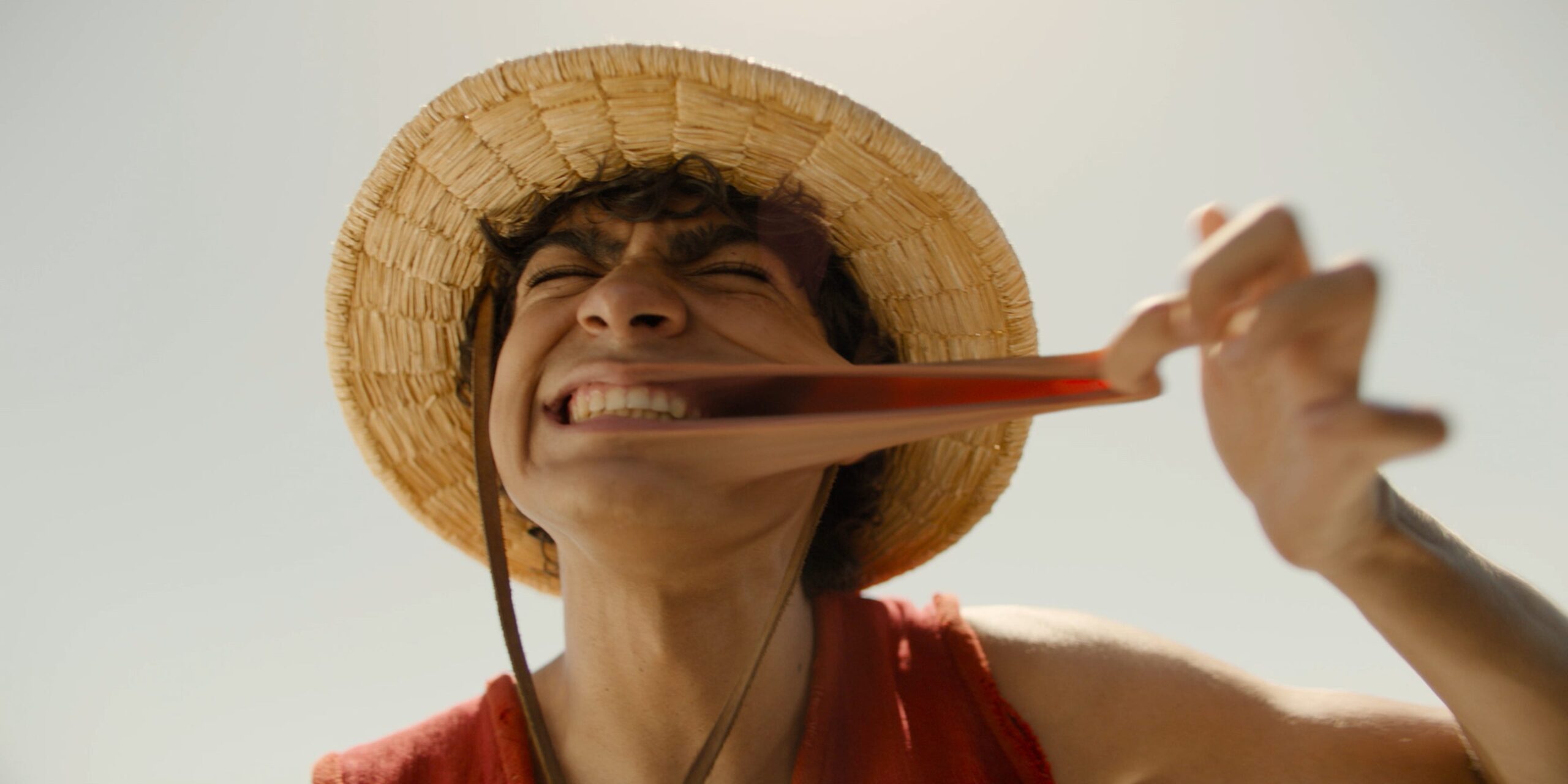 iñaki godoy as luffy in netflix's one piece. he's stretching out his cheek, demonstrating that he can stretch like rubber, and grinning widely