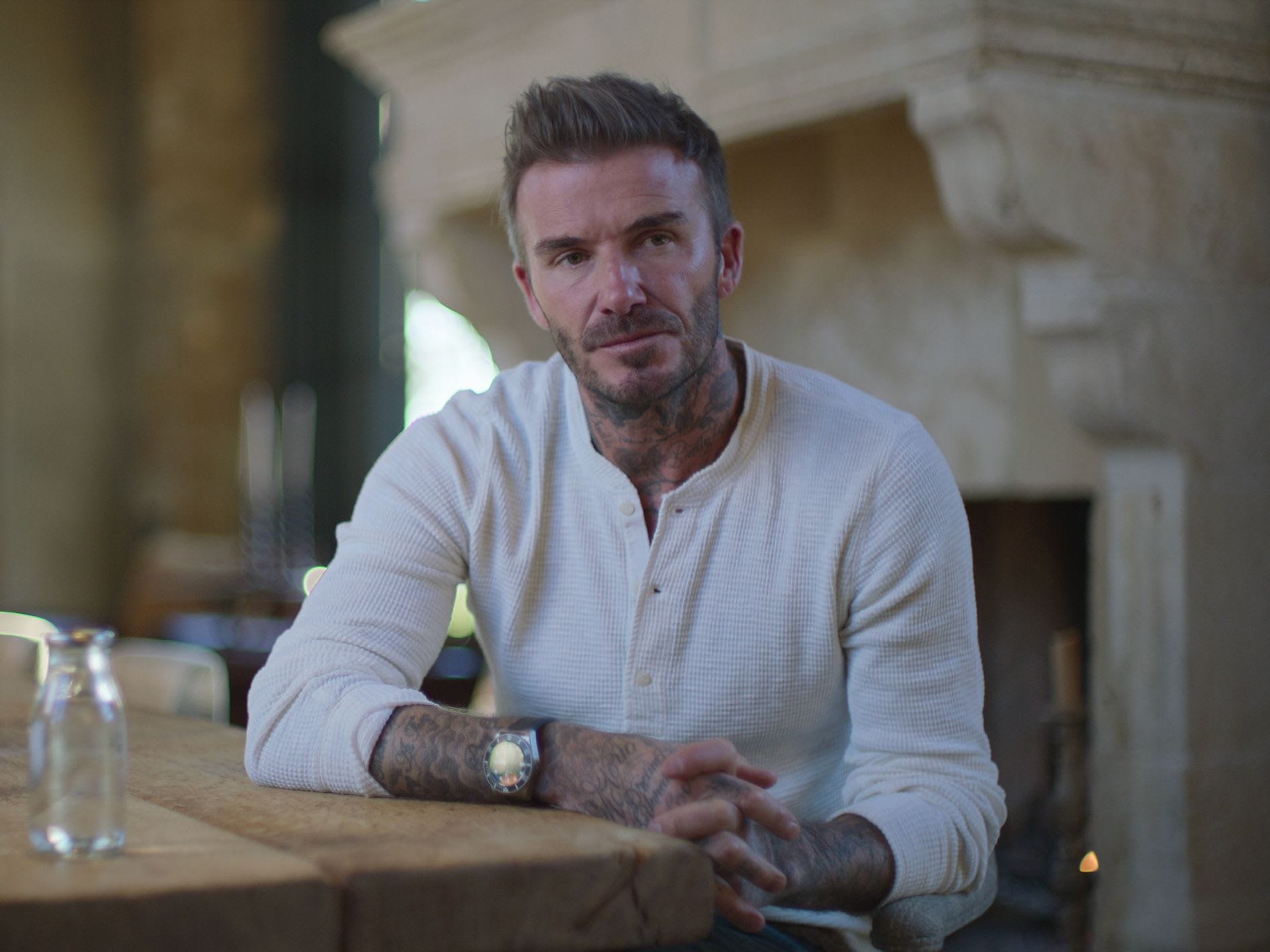 david beckham sitting at a bar, one arm resting on the wood. he's looking into the distance pensively