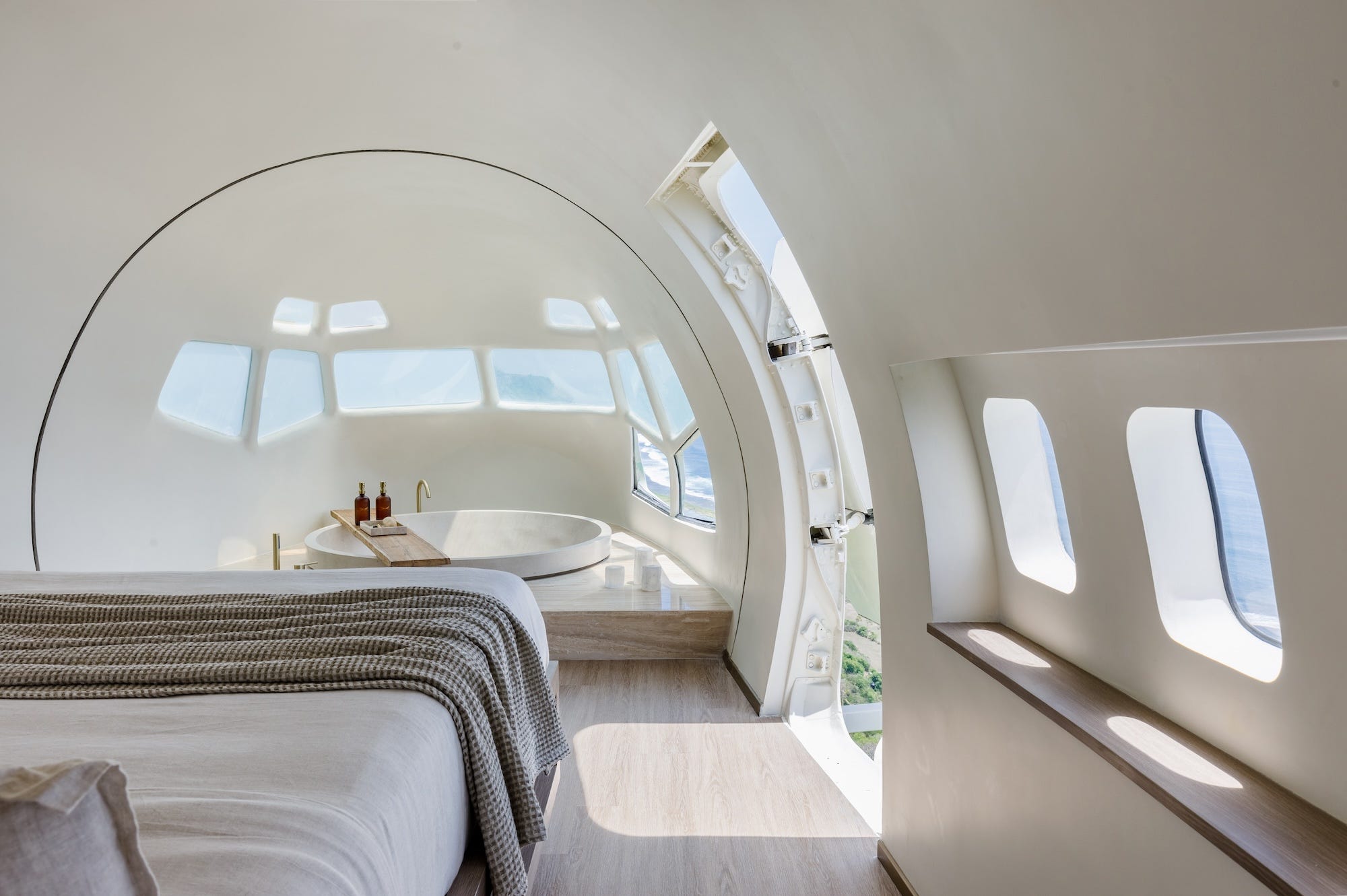 Een bed kijkt uit op de jacuzzi ingebouwd in een slaapkamer. Ramen vullen de ronde ruimte.