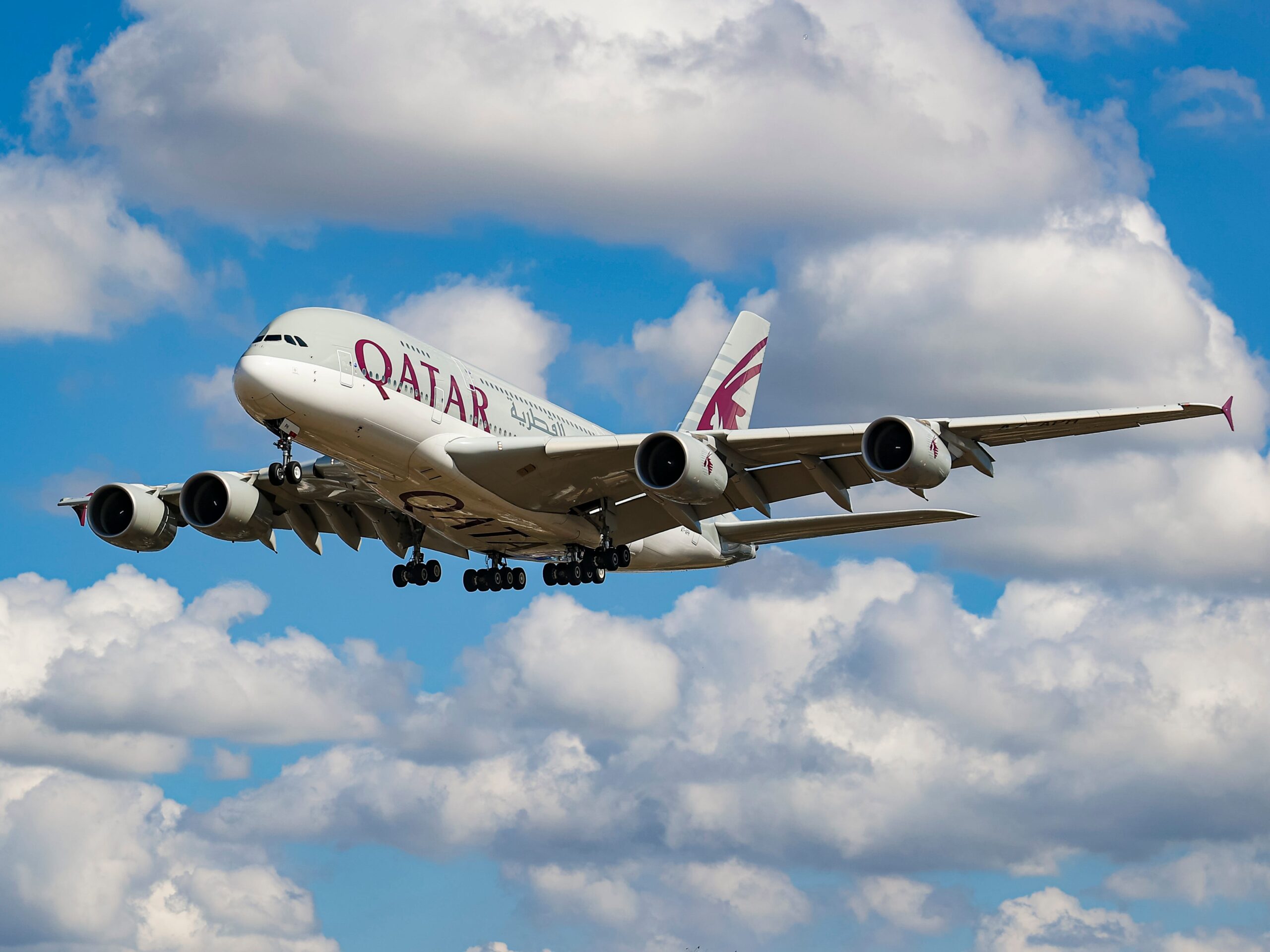 A Qatar flight in the air with clouds above it