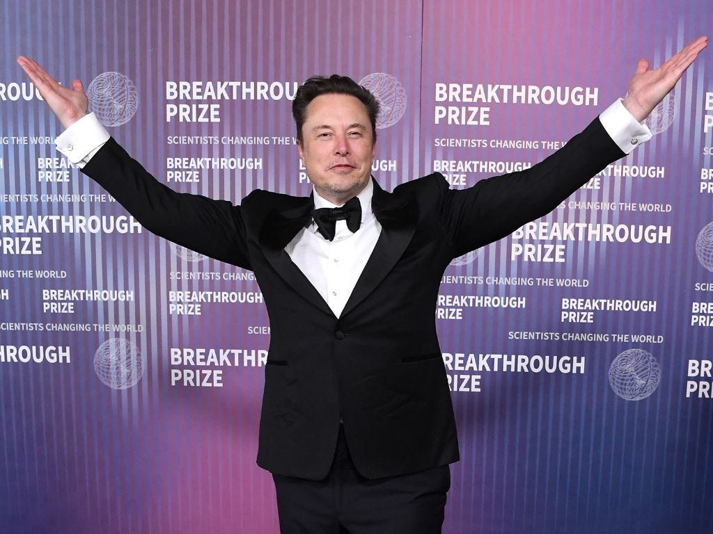 Elon Musk is wearing a tuxedo with his hands raised in the air.