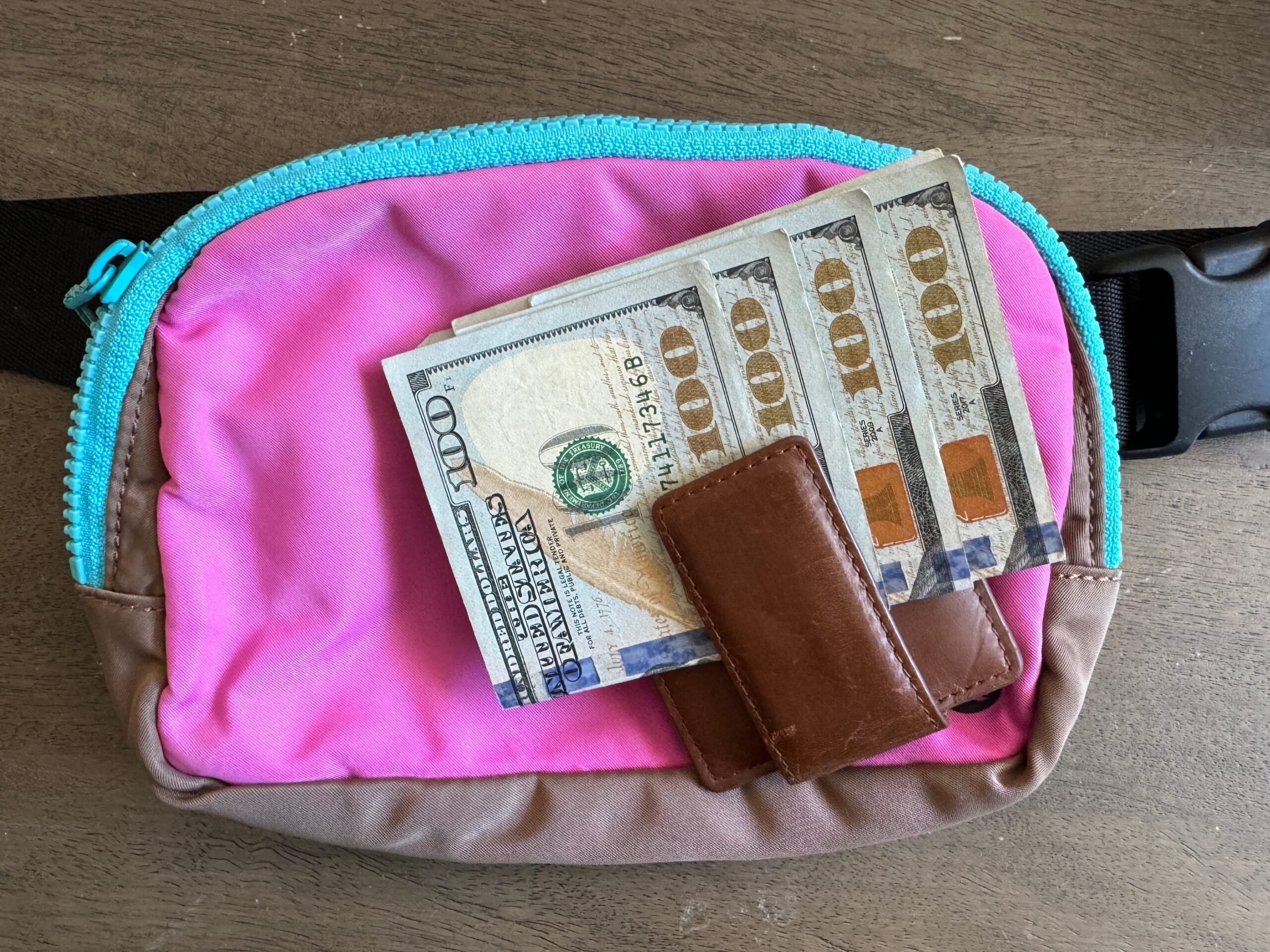 wallet full of $100 dollar bills on top of a crossbody bag