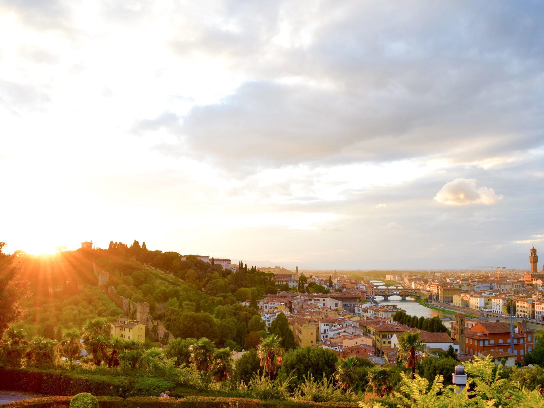 An aerial view of houses and mountains in Florence, Italy, with the sun shining in the sky.