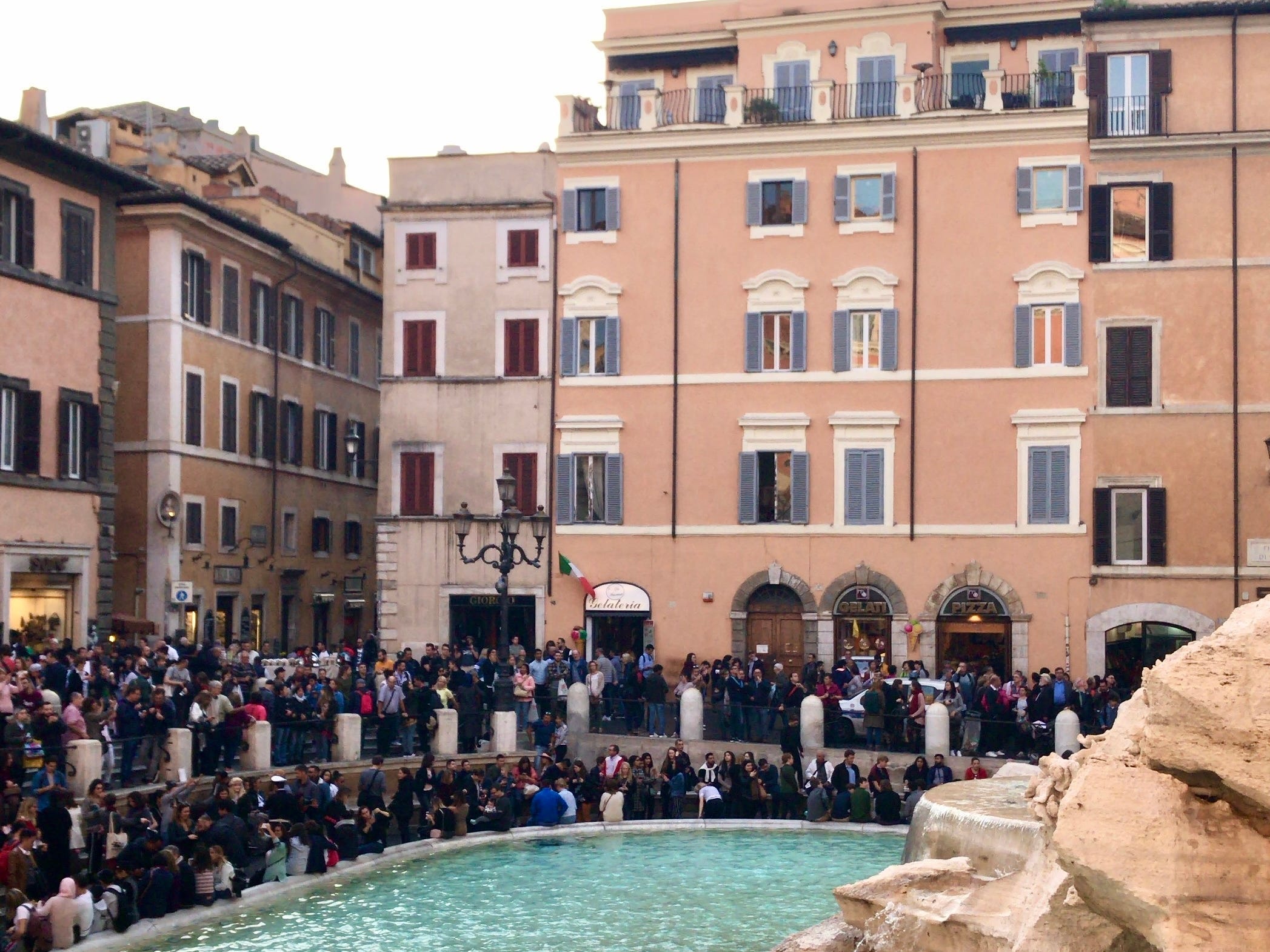 Crowds of people surrounding Rome's Trevi Fountain and buildings in Italy.