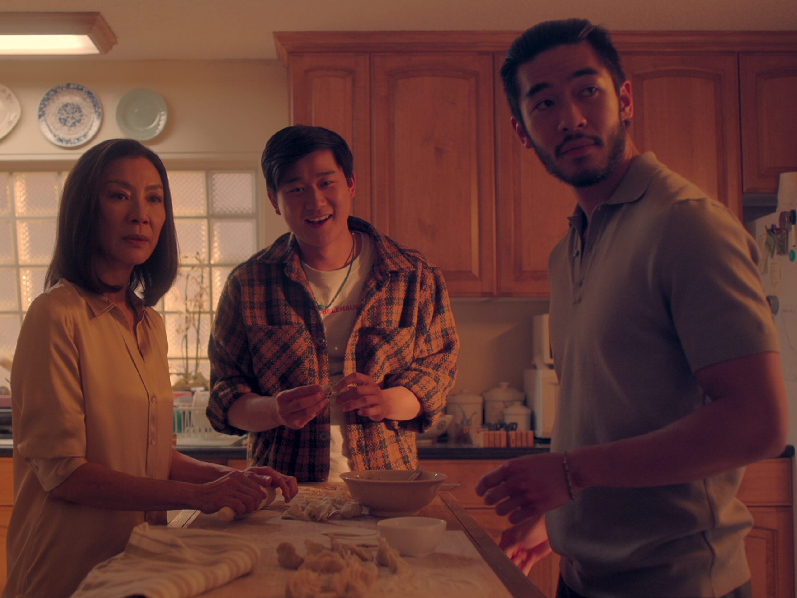 mama sun, bruce sun, and charles sun in the brothers sun, standing around a kitchen island making dumplings