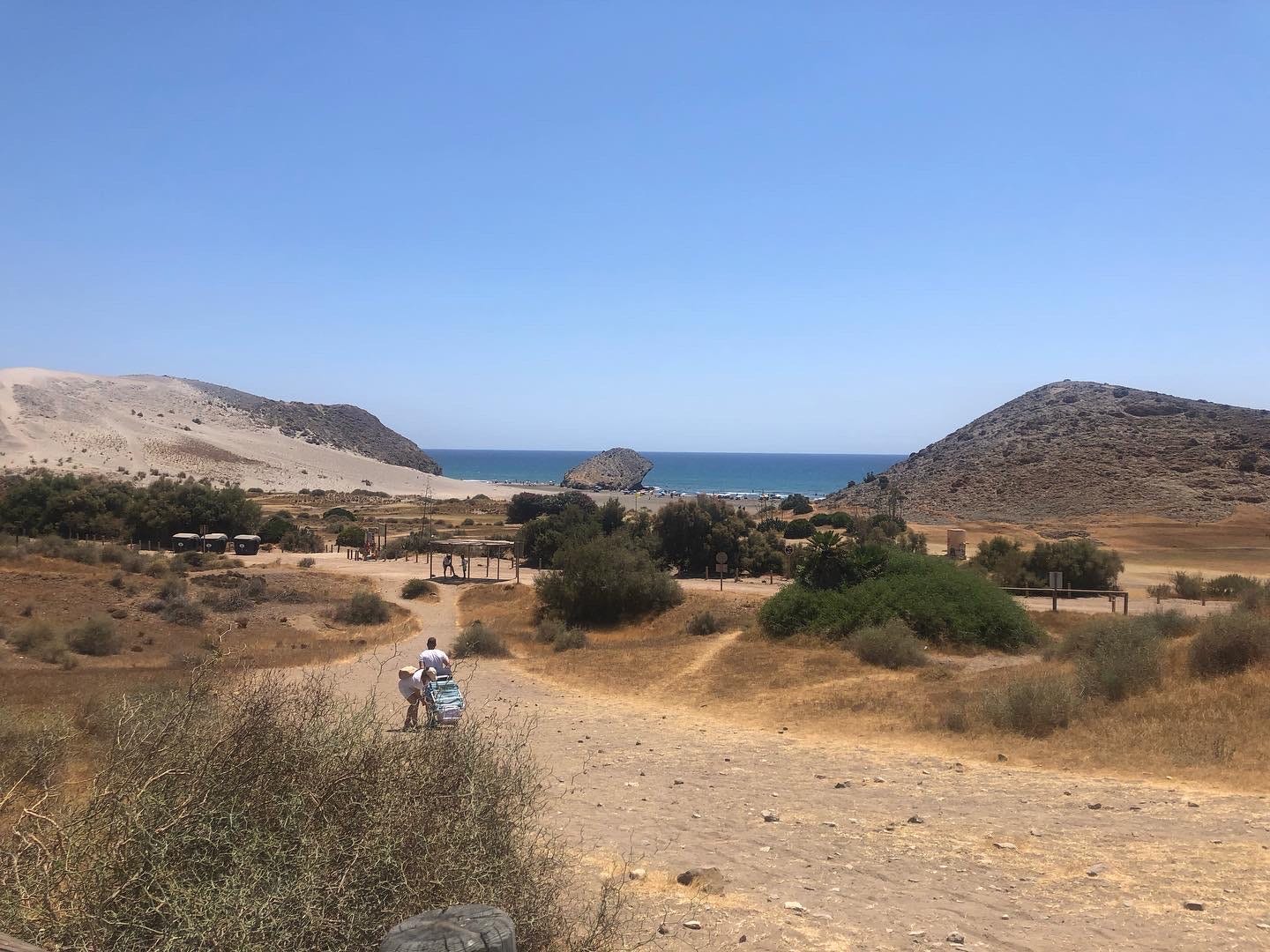 The Cabo de Gata-Níjar in Spain featuring a sand path with hills and a body of water in the background.