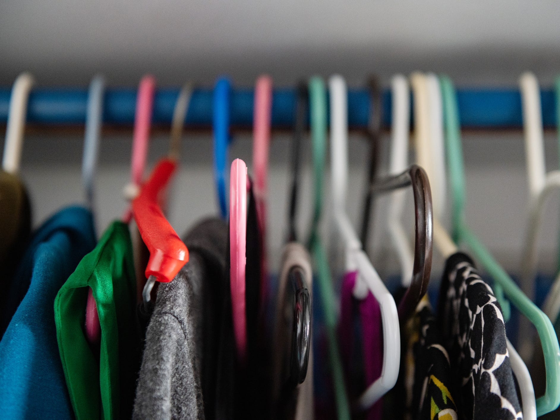 Clothing on different colored plastic hangers.